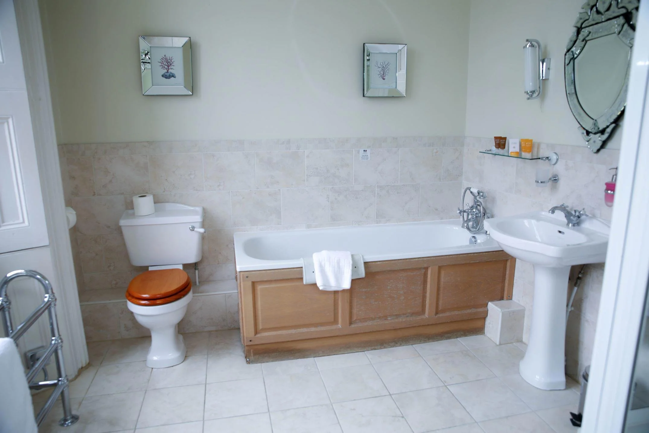Bathroom with bathtub, toilet, pedestal sink, and wall art.