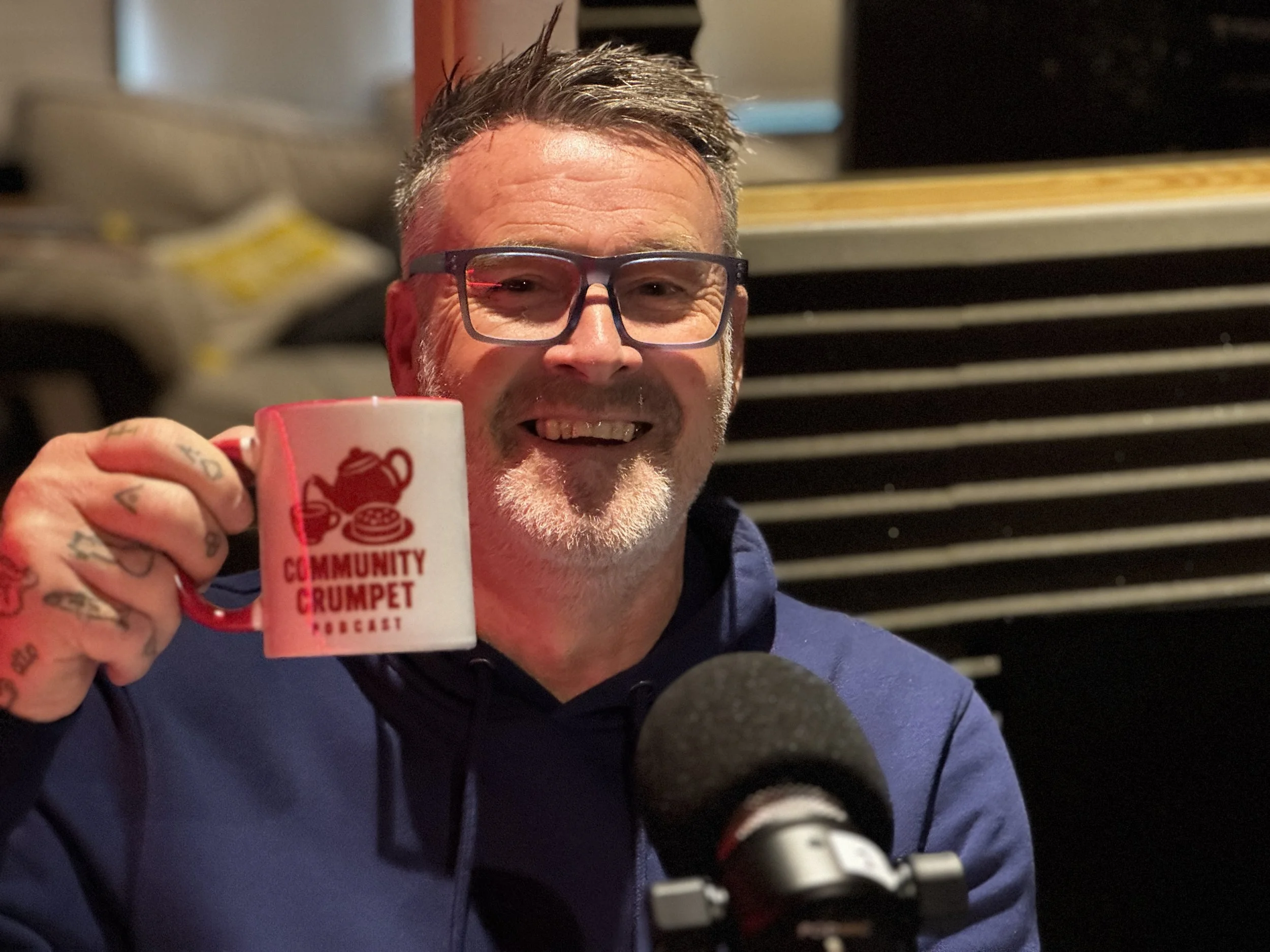 Tony Callister Community Crumpet Podcast Host Smiling At Camera Holding A White Mug With Community Crumpet Logo