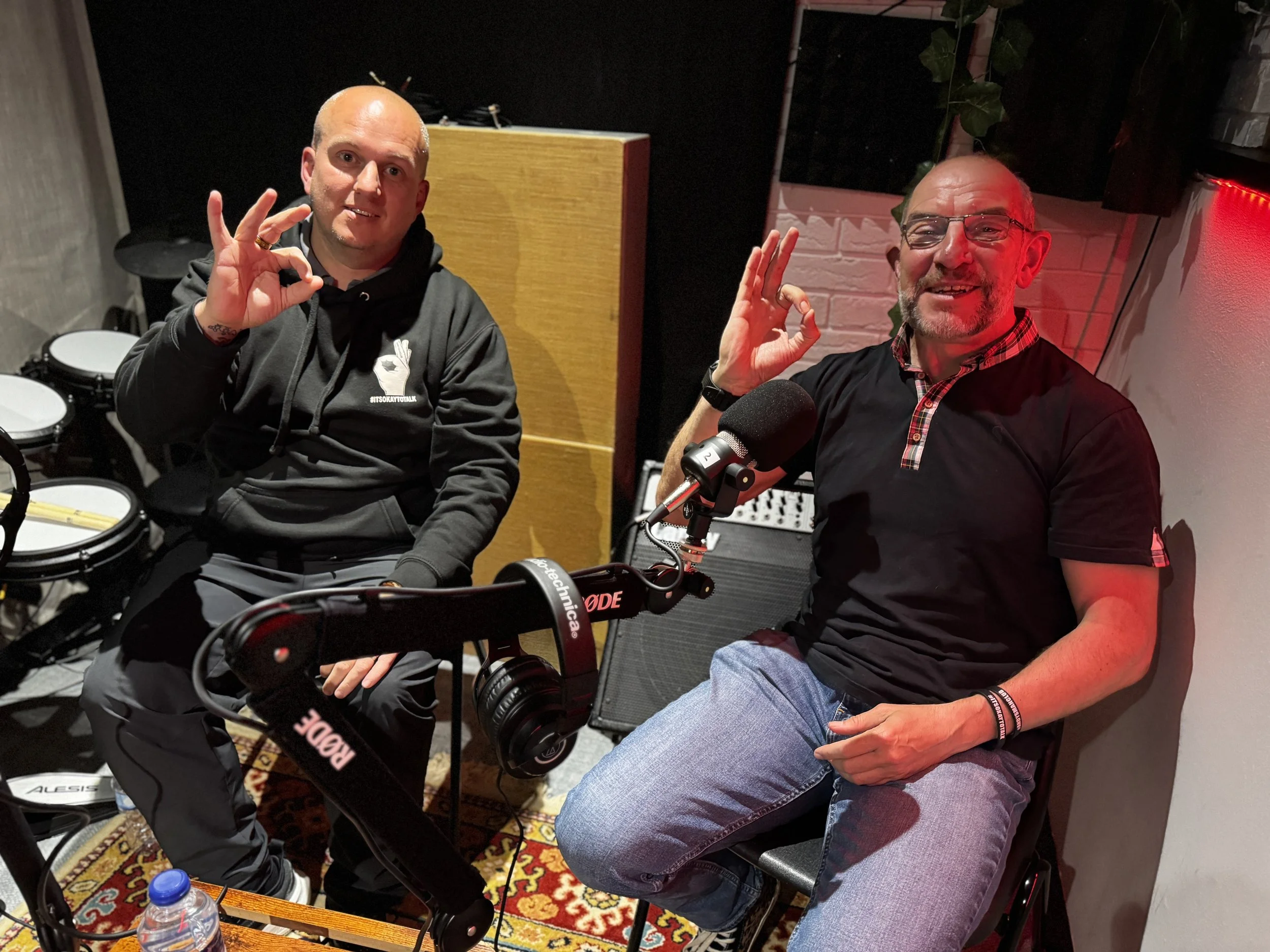 Two Men From Andy's Man Club Barrow in Furness Holding up ok hand symbol smiling at camera in the community crumpet podcast recording studion