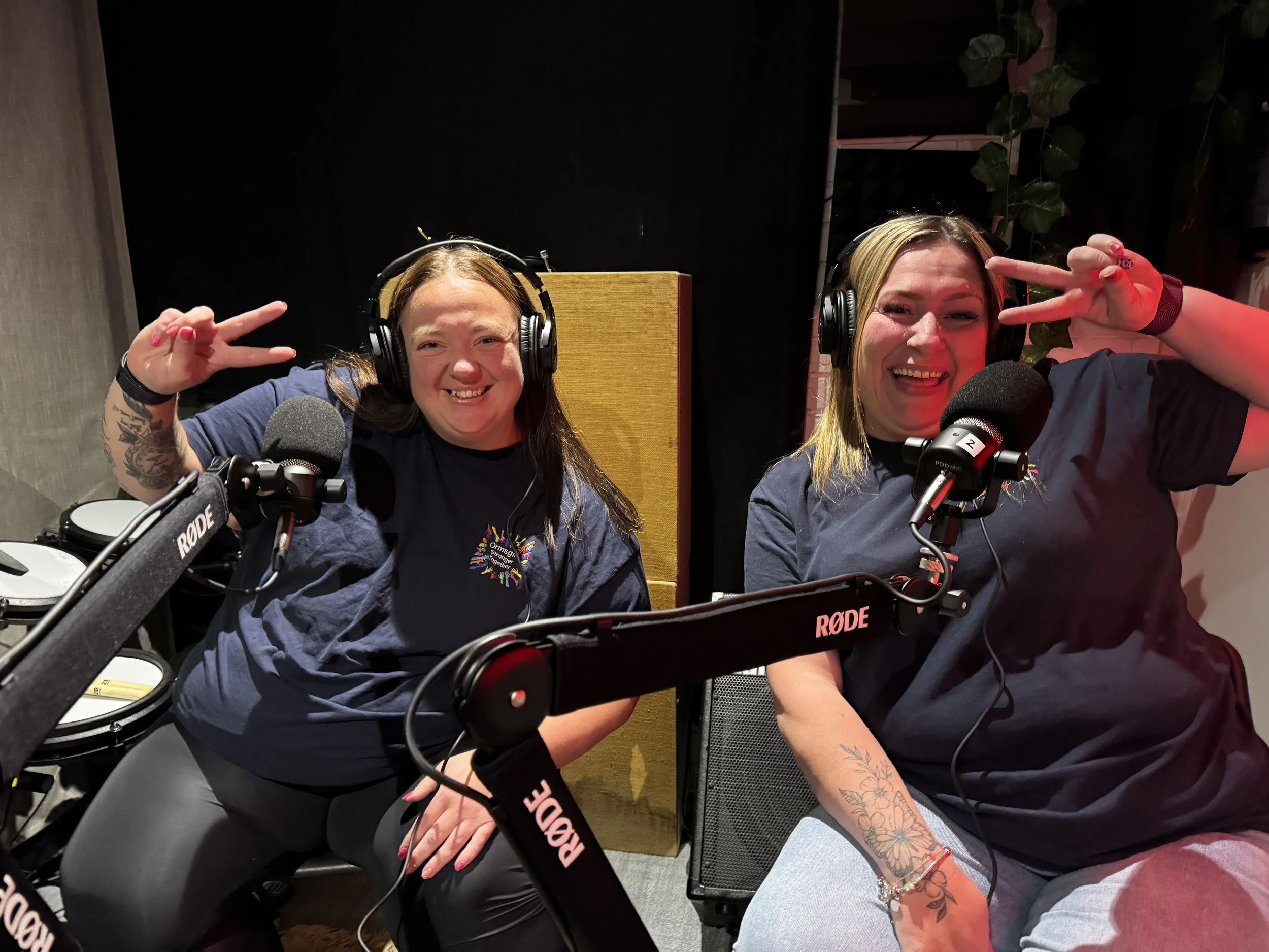 Two Ladies from Ormsgill Stronger Together holding peace signs up at camera whilst laughing in community crumpet podcast recording studio