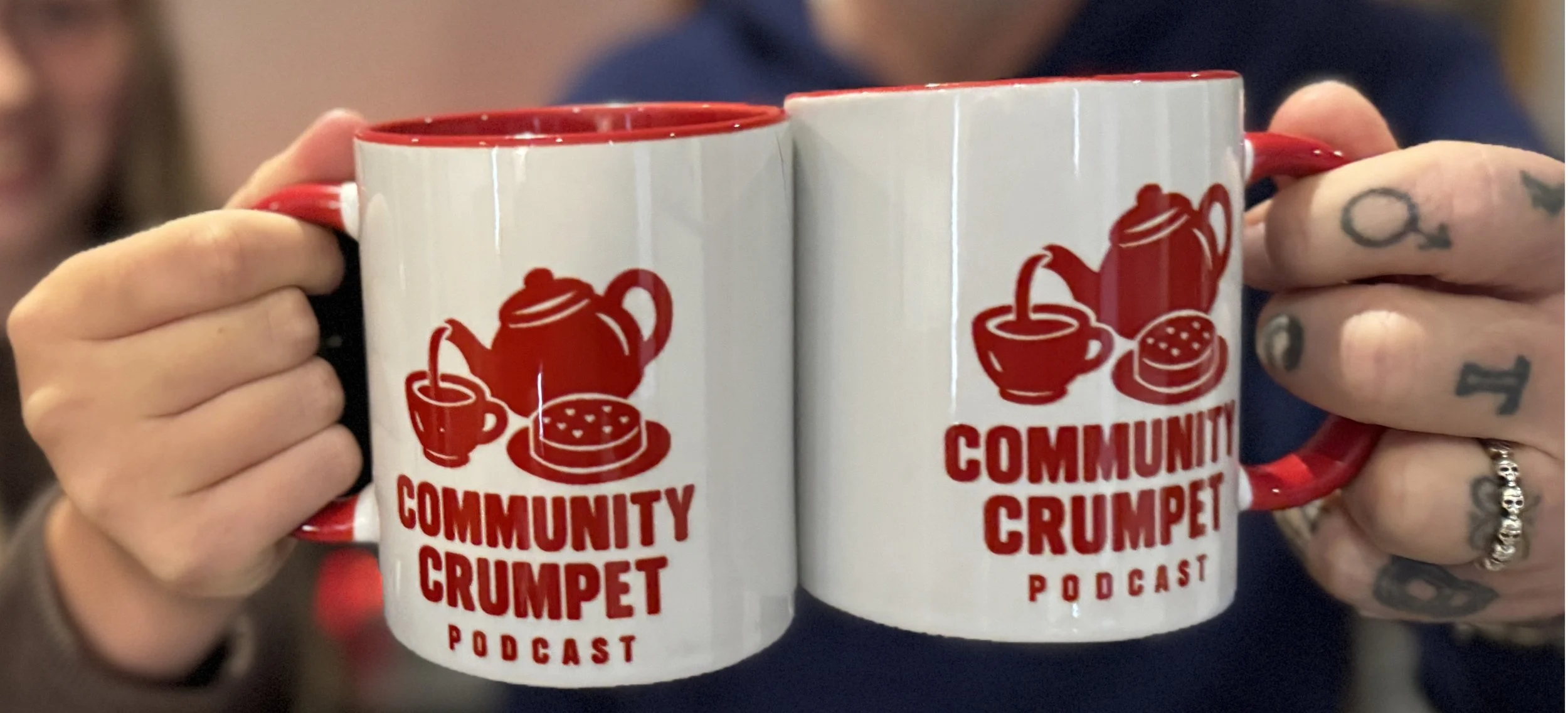 Two Community Crumpet Podcast Mugs featuring the Community Crumpet Podcast Red Logo of Teapot pouring into a mug with a crumpet nearby with hearts on top. The mugs are held by Tony Callister podcast host on the right and a young girl on the left
