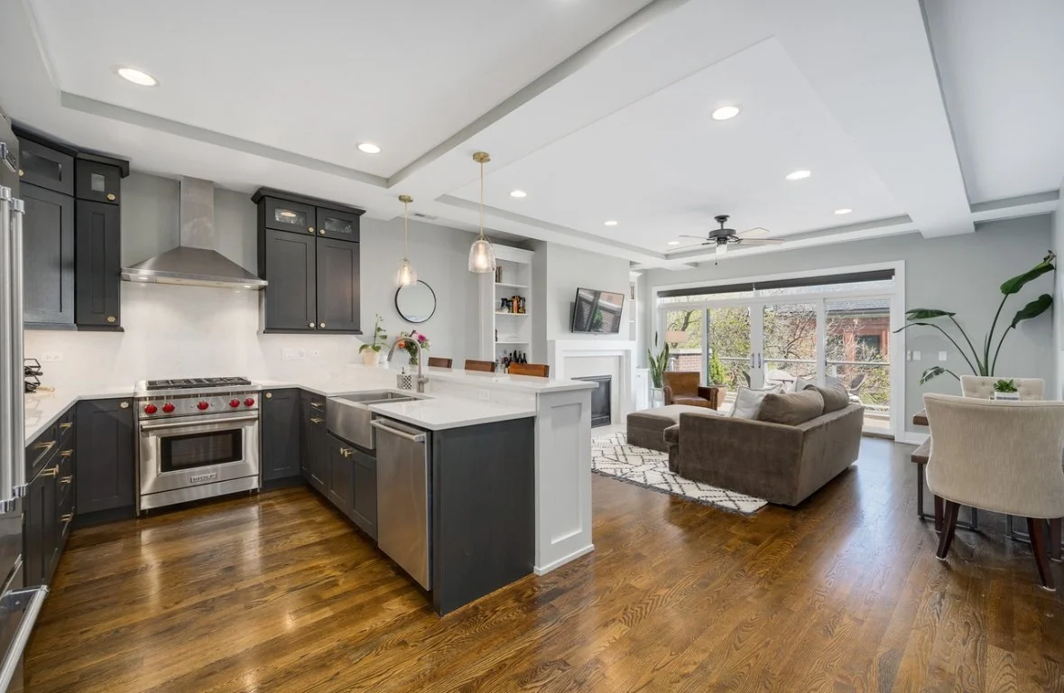 Open-concept living room and kitchen with hardwood floors, black kitchen cabinets, stainless steel appliances, and a sliding glass door leading to a balcony.