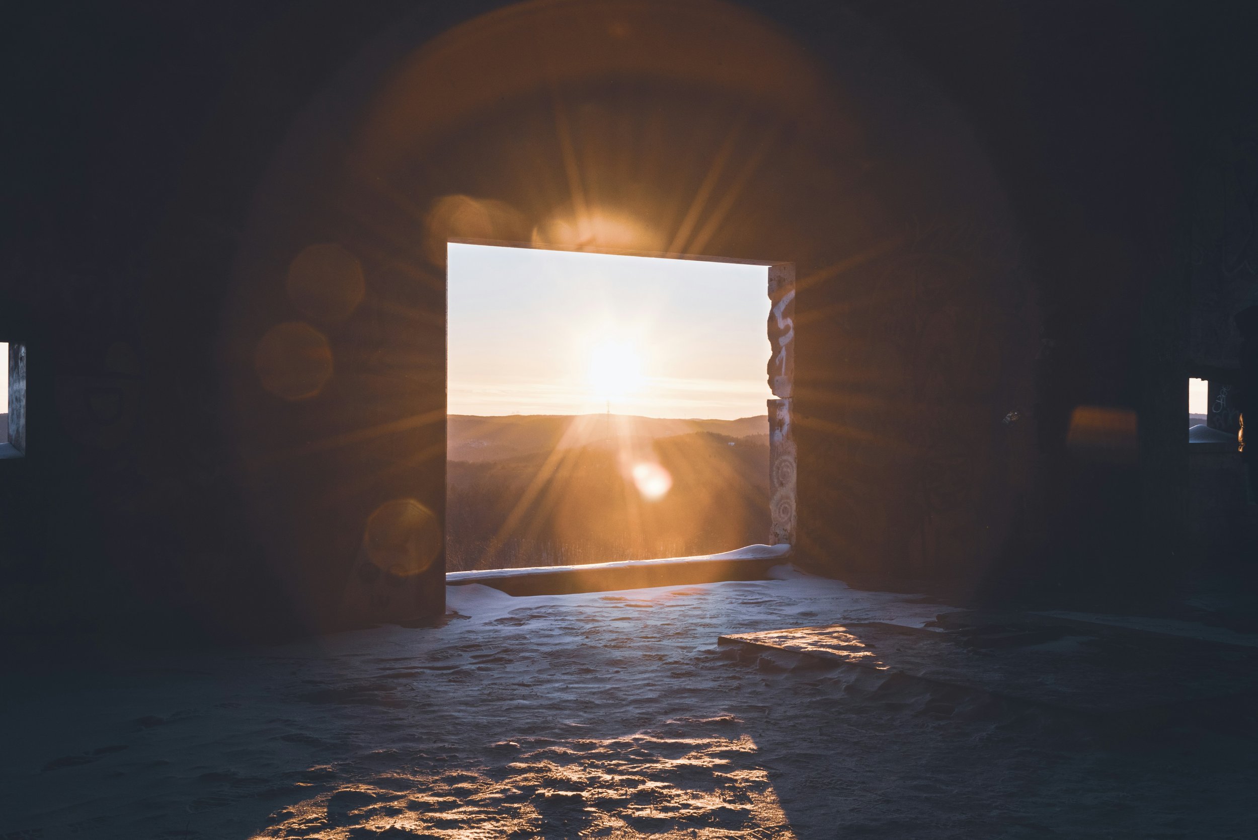 Sunset viewed through an opening in a rocky structure with a sandy ground inside.
