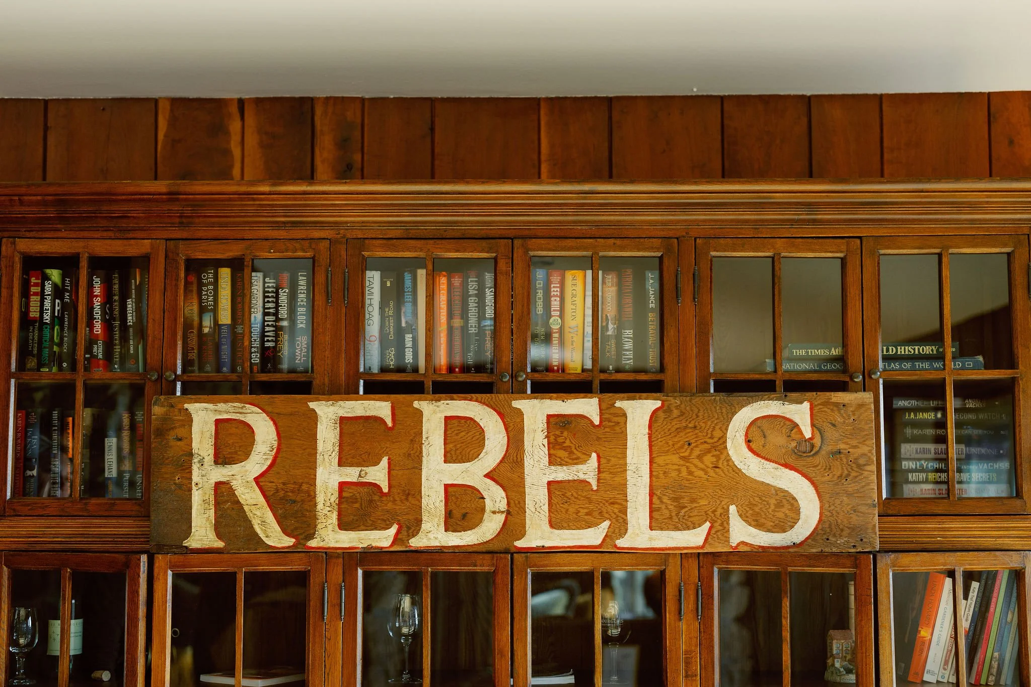 A wooden cabinet filled with books and knick-knacks, with a large wooden sign that says 'REBELS' in white letters with red outlines across the middle of the cabinet.