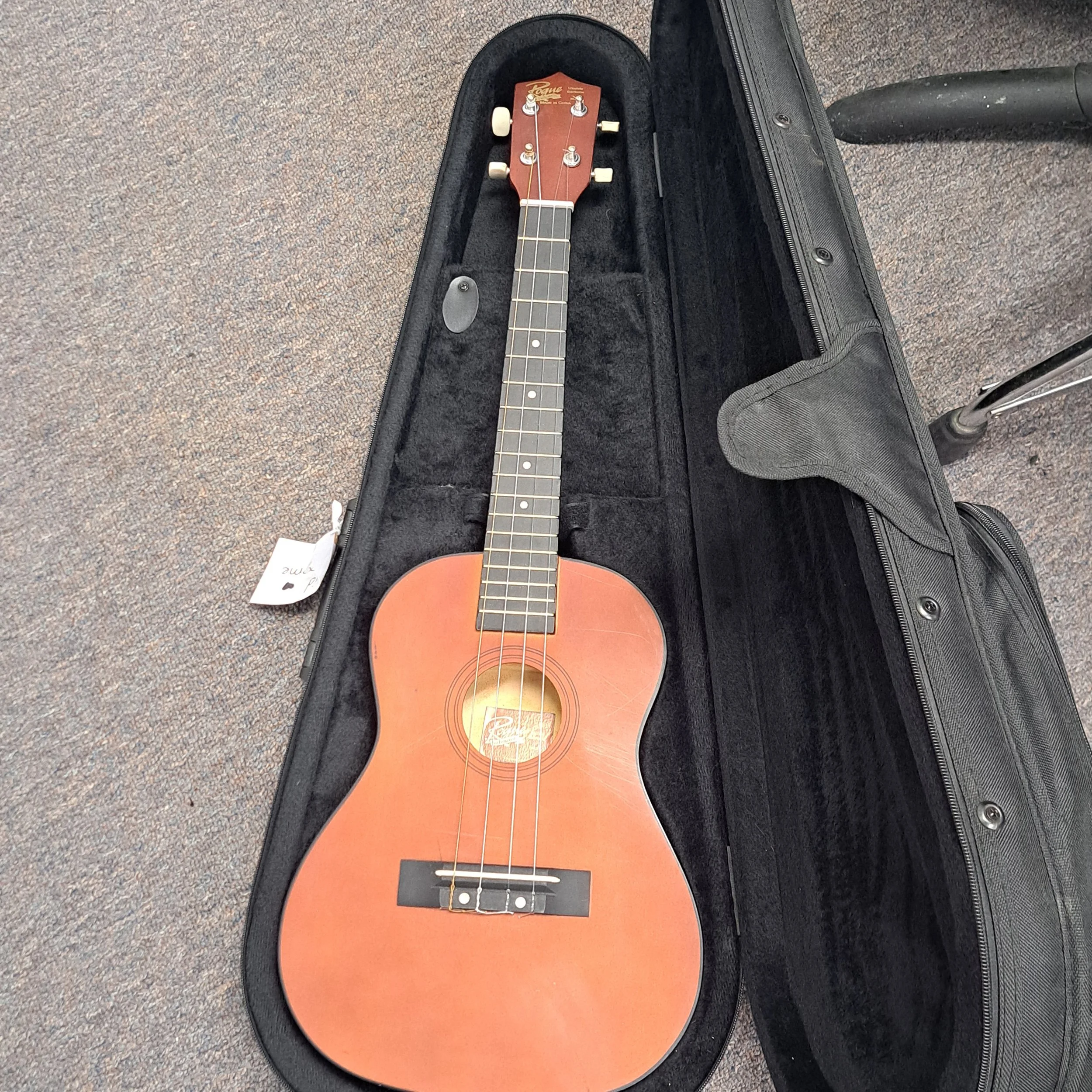 An acoustic guitar inside an open black guitar case on a speckled gray carpet.