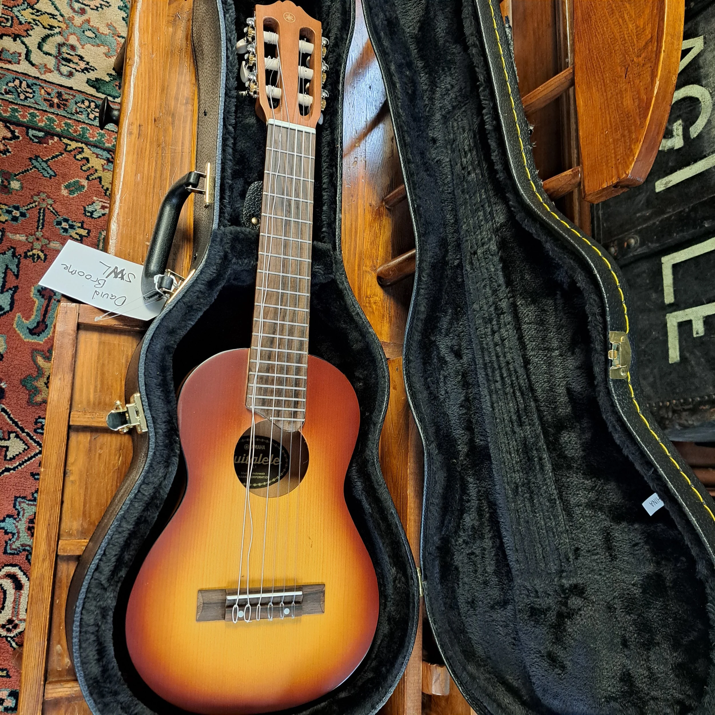 An acoustic guitar in an open black case on a wooden table with a patterned rug nearby.