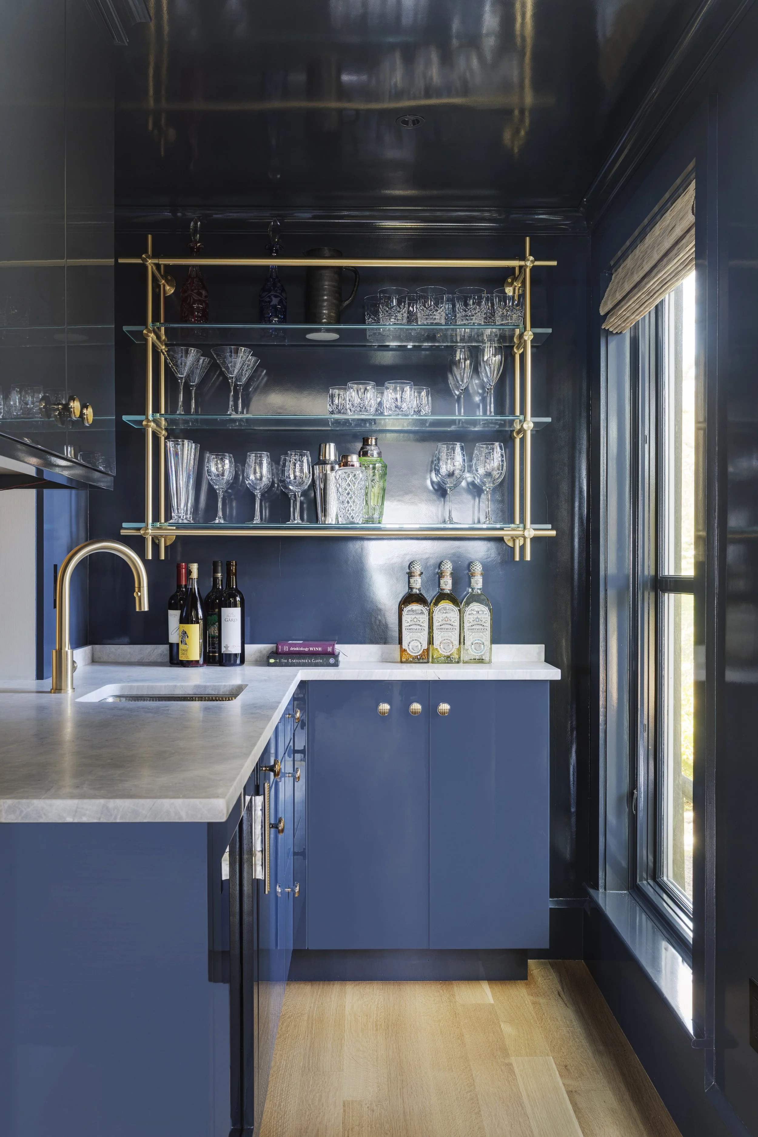 High gloss navy cabinetry, custom wet bar with brass hardware and glass shelves
