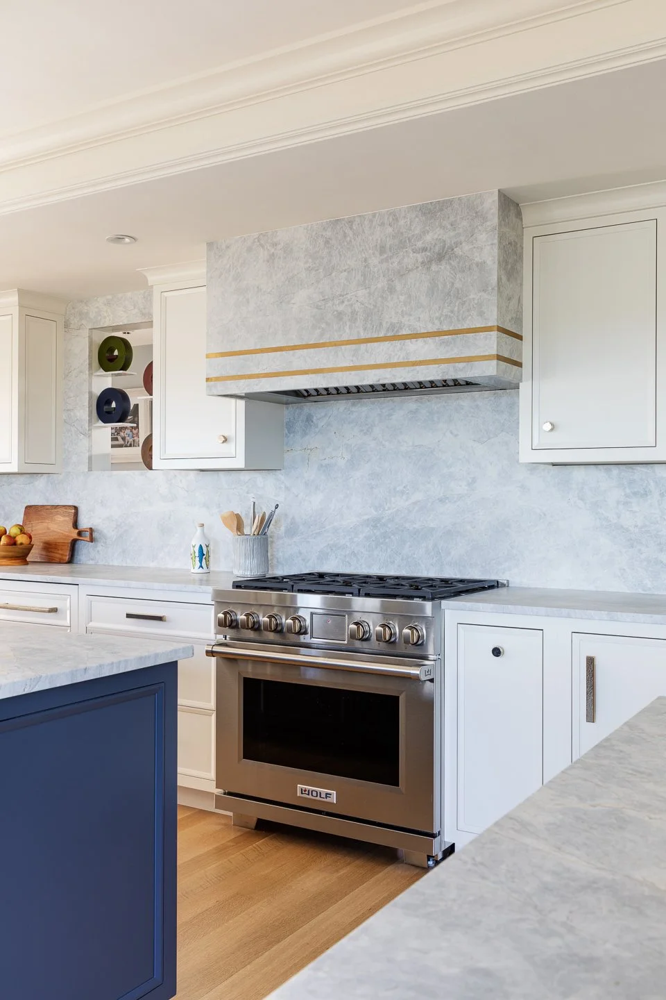 white cabinetry with navy island and full height backsplash and stone hood