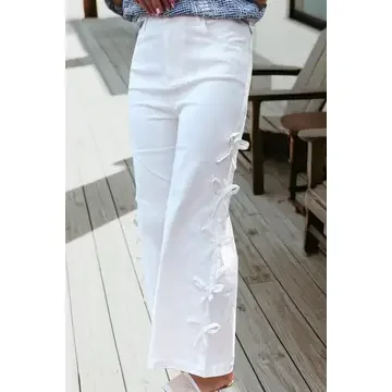 Person wearing white trousers with embroidered bow designs standing on wooden floor near chairs.