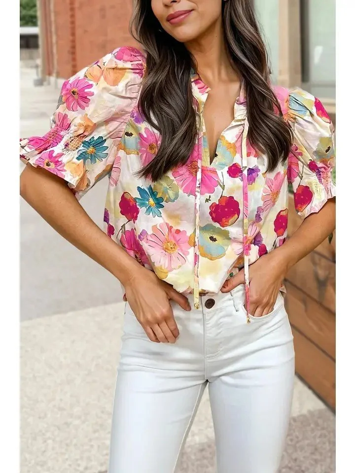 A woman wearing a colorful floral blouse with puffed sleeves and white pants.