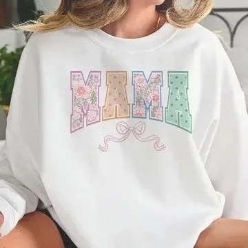 A woman wearing a white sweatshirt with the word 'MAMA' in large, colorful, patterned letters.