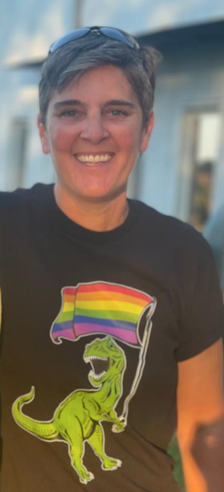 Head shot of Ali wearing a tee-shirt of a T-Rex holding a Pride flag