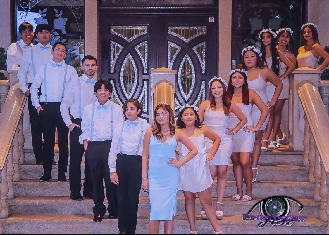 Group of young people dressed in formal attire on a staircase outside a building, posing for a photo at a celebration or event.
