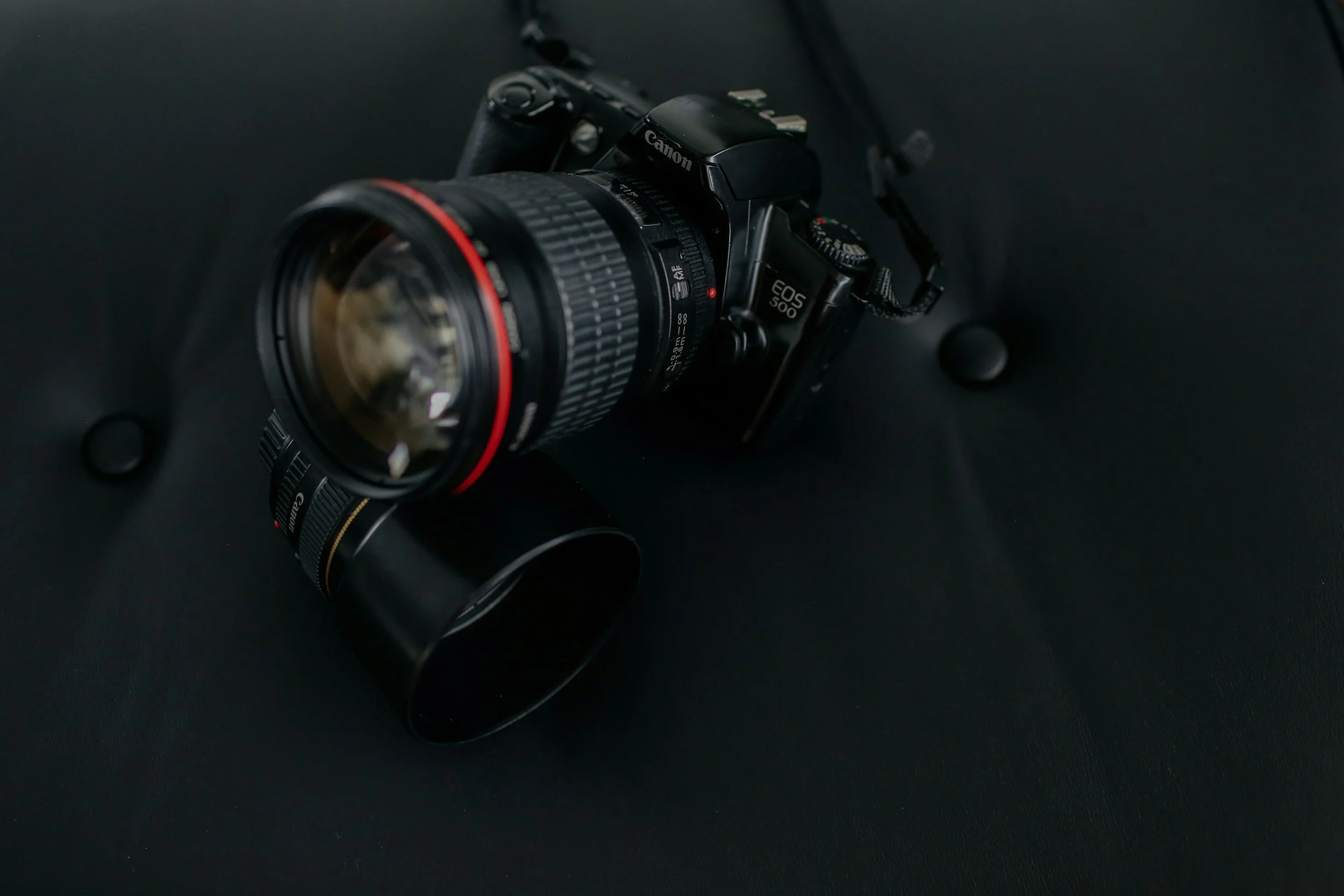 A Canon EOS 5D Mark IV camera with a large zoom lens attached, placed on a black surface.