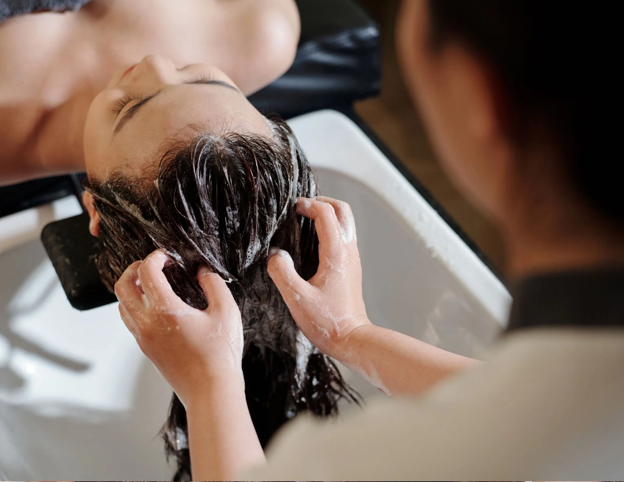 A person getting their hair washed in a salon sink with a stylist washing their hair.