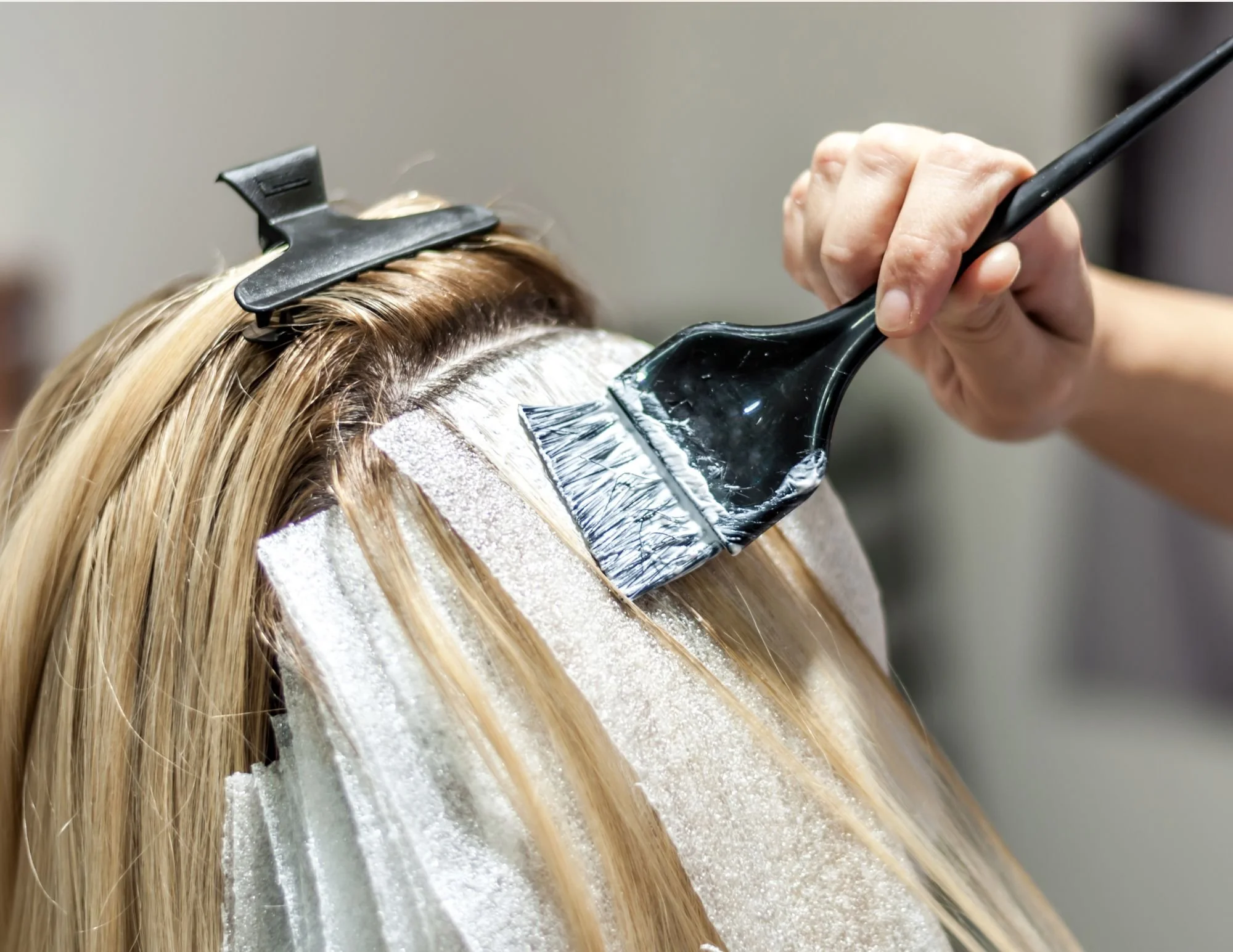 Hairdresser applying hair dye with a brush and foil highlights.