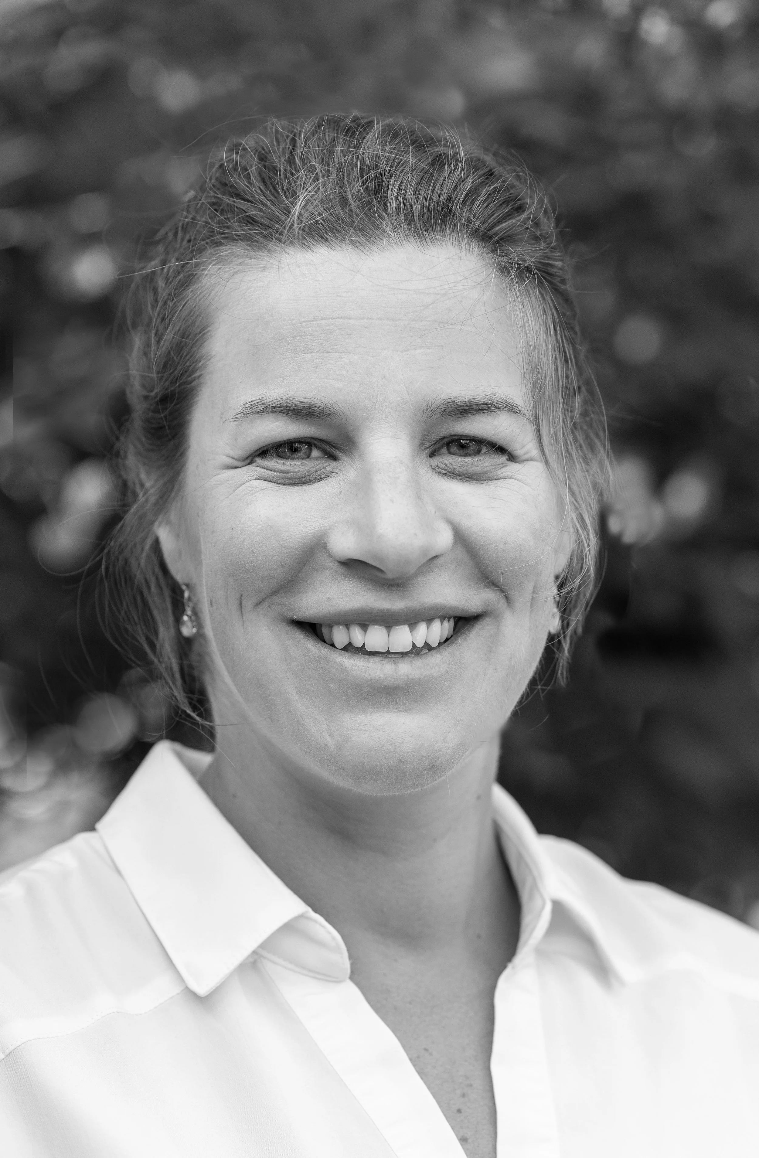 Jess Damon, associate at Ascend Group, smiling with wavy light hair pulled back, wearing a white collared shirt outdoors.