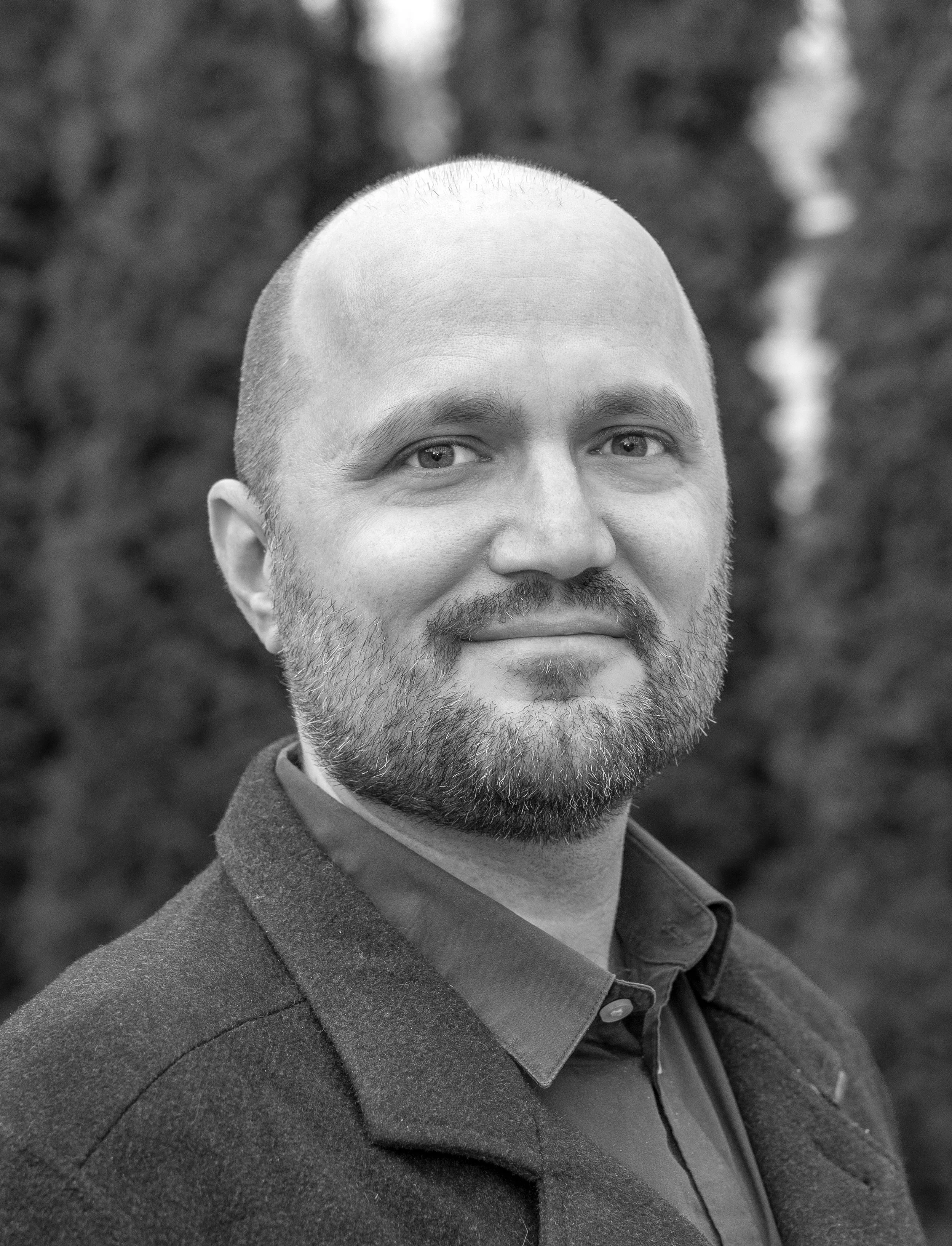 Justin Sargent, Associate at Ascend Group, bald with short beard, wearing a collared coat and shirt outdoors.