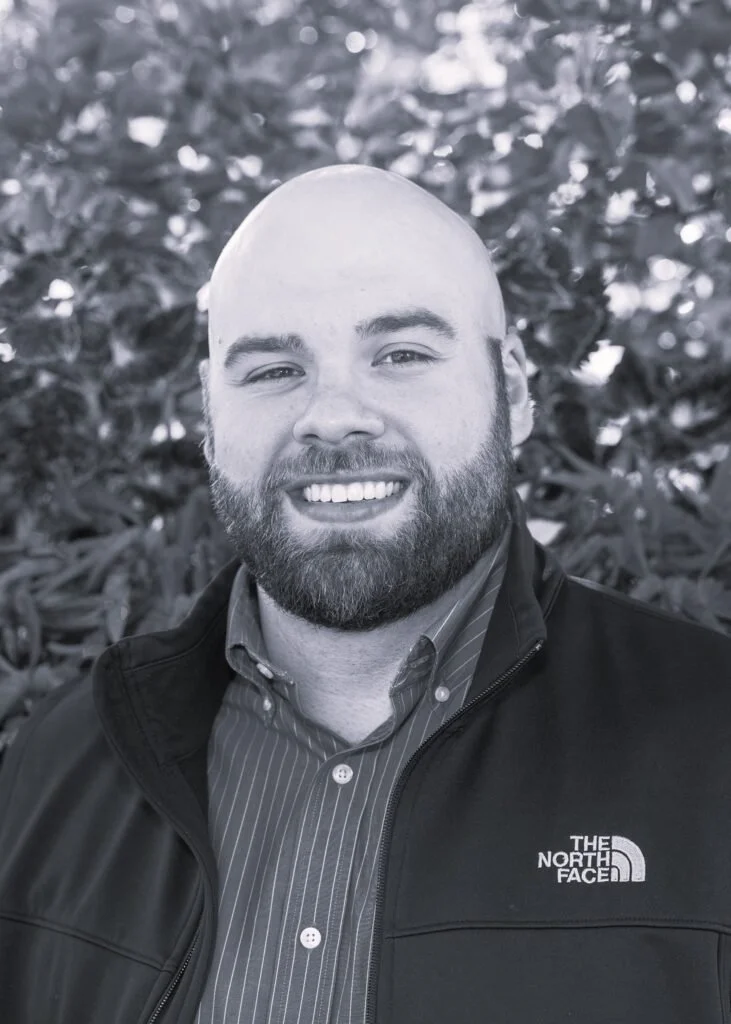 Ryan Robbins, associate at Ascend Group, bald with a short beard, wearing a striped collared shirt and North Face jacket outdoors.