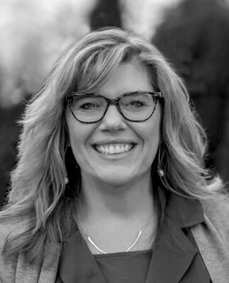 Deb di Stefano, associate at Ascend Group, with wavy light hair and glasses, smiling in a blazer outdoors.