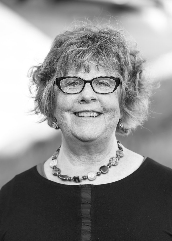 Ki McClennan, associate at Ascend Group, with short wavy light hair, wearing glasses, a beaded necklace, and dark top outdoors.