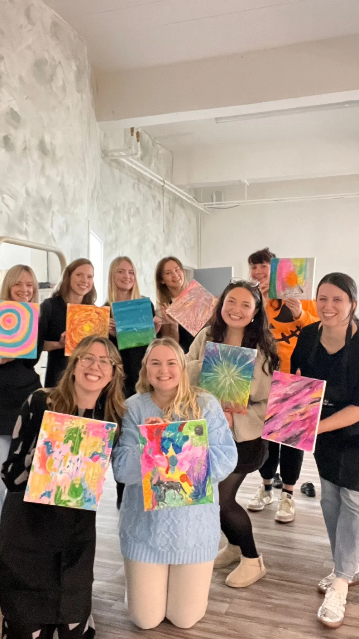 A group of women holding up colourful paintings after a workshop with Calm and Canvas in Glasgow