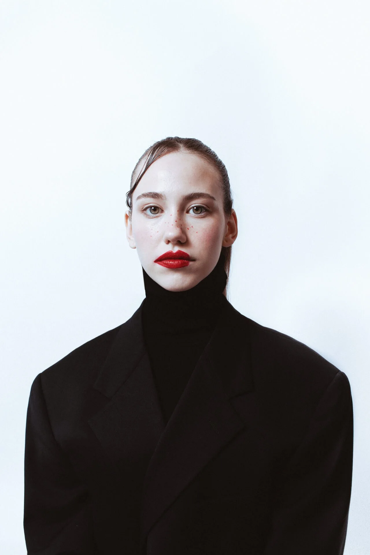 Ritratto editoriale di ragazza bionda con giacca nera e collo alto e rossetto rosso