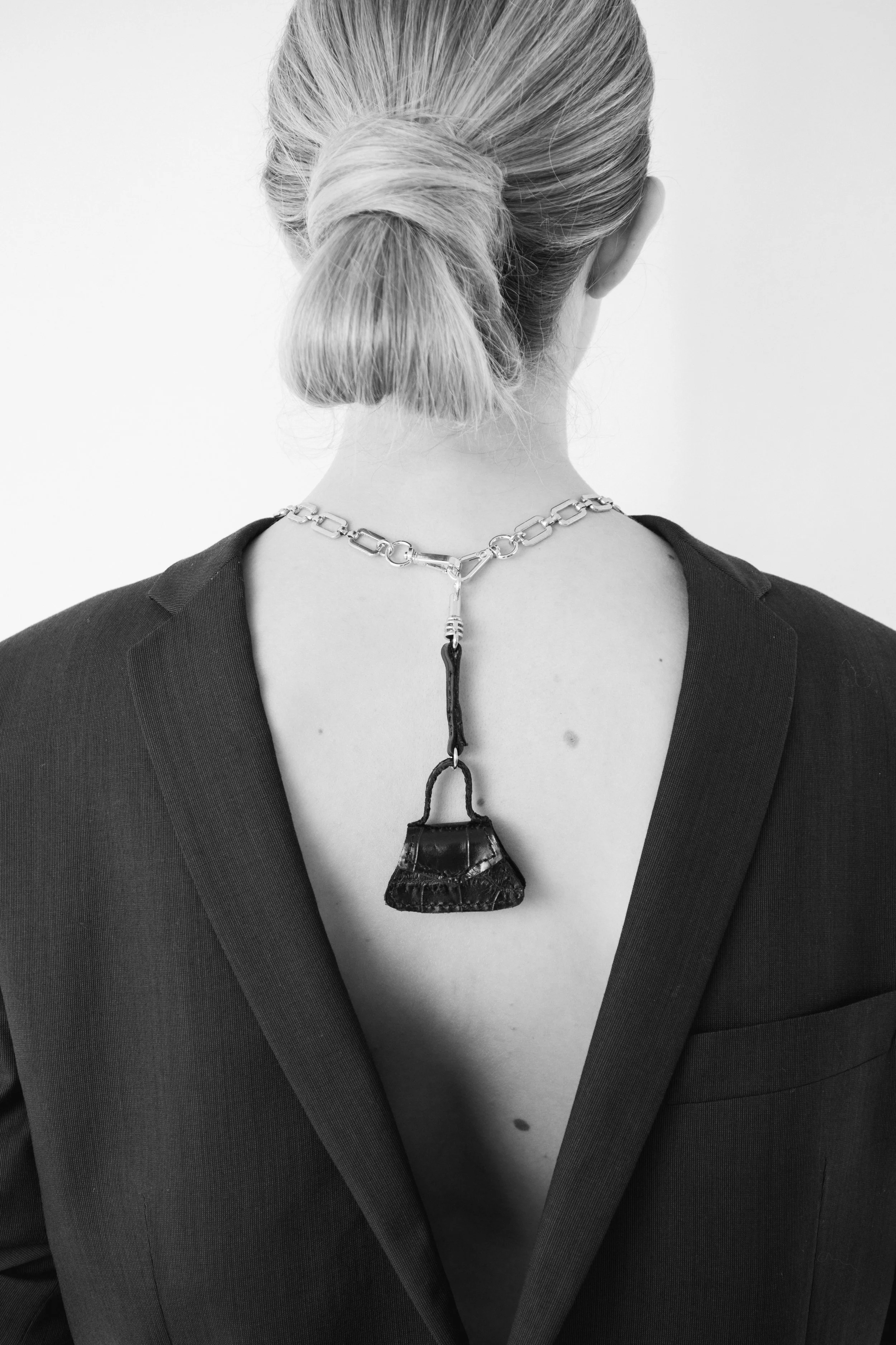 Ritratto editoriale in bianco e nero di ragazza bionda con blazer nero e una borsa mini Bistrusso