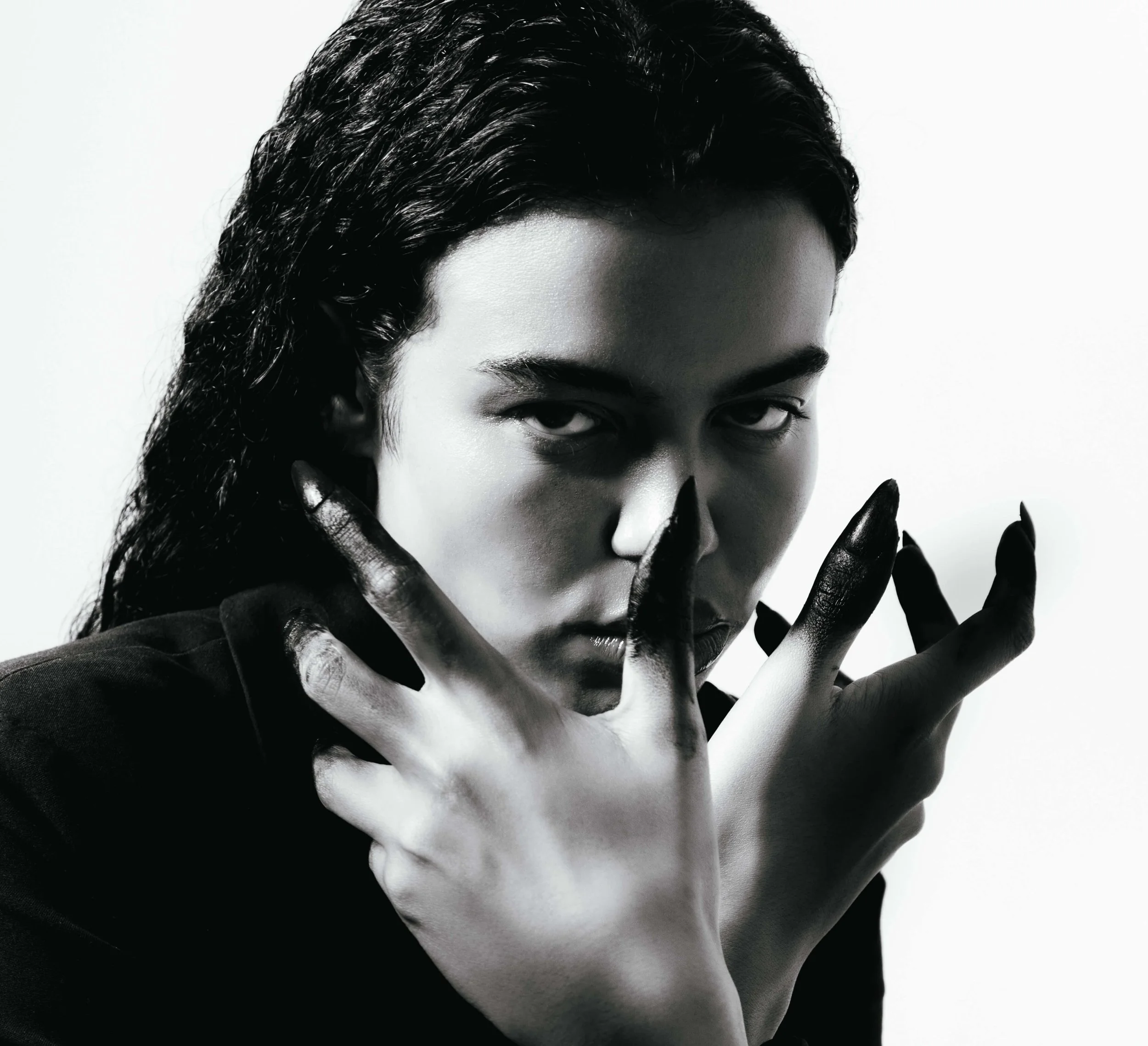 Primo piano in bianco e nero su sfondo bianco di ragazza con i capelli neri e le dita macchiate di nero stile Rick Owens