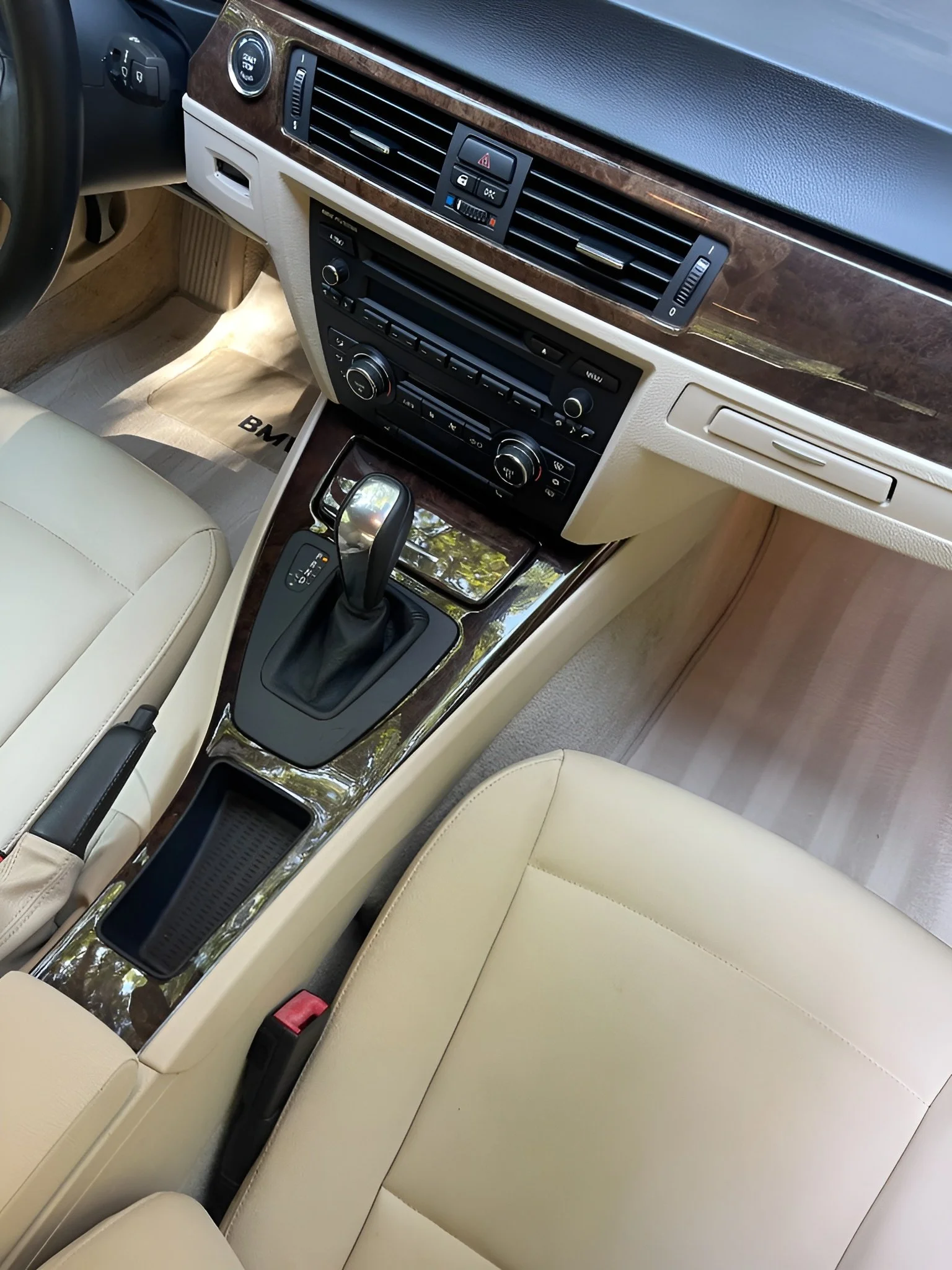 Interior of a luxury car with beige leather seats, a wooden center console with a gear shifter, and an dashboard with climate controls and air vents.