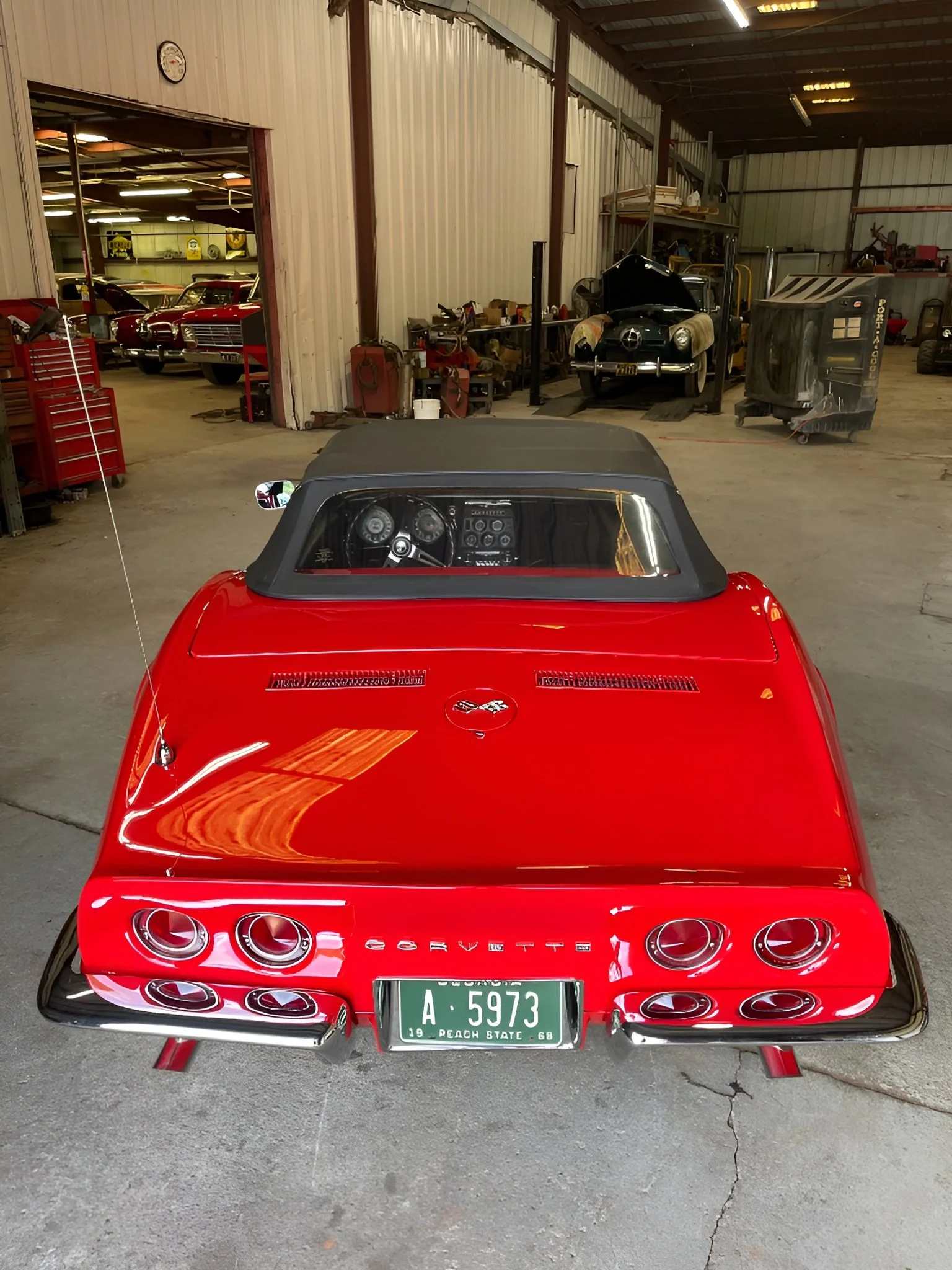Red Chevrolet Corvette convertible inside a garage, with classic cars visible in the background.