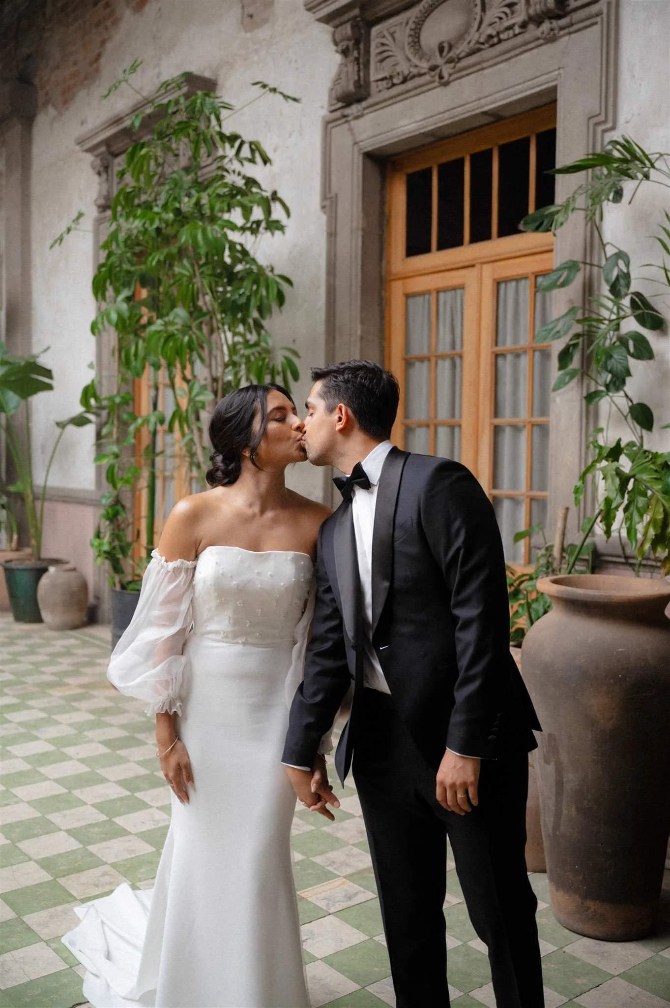 Bride and groom sharing a kiss at Proyectos Públicos: Prim in Mexico City, with tropical plants and vibrant floral decor creating an intimate wedding atmosphere.