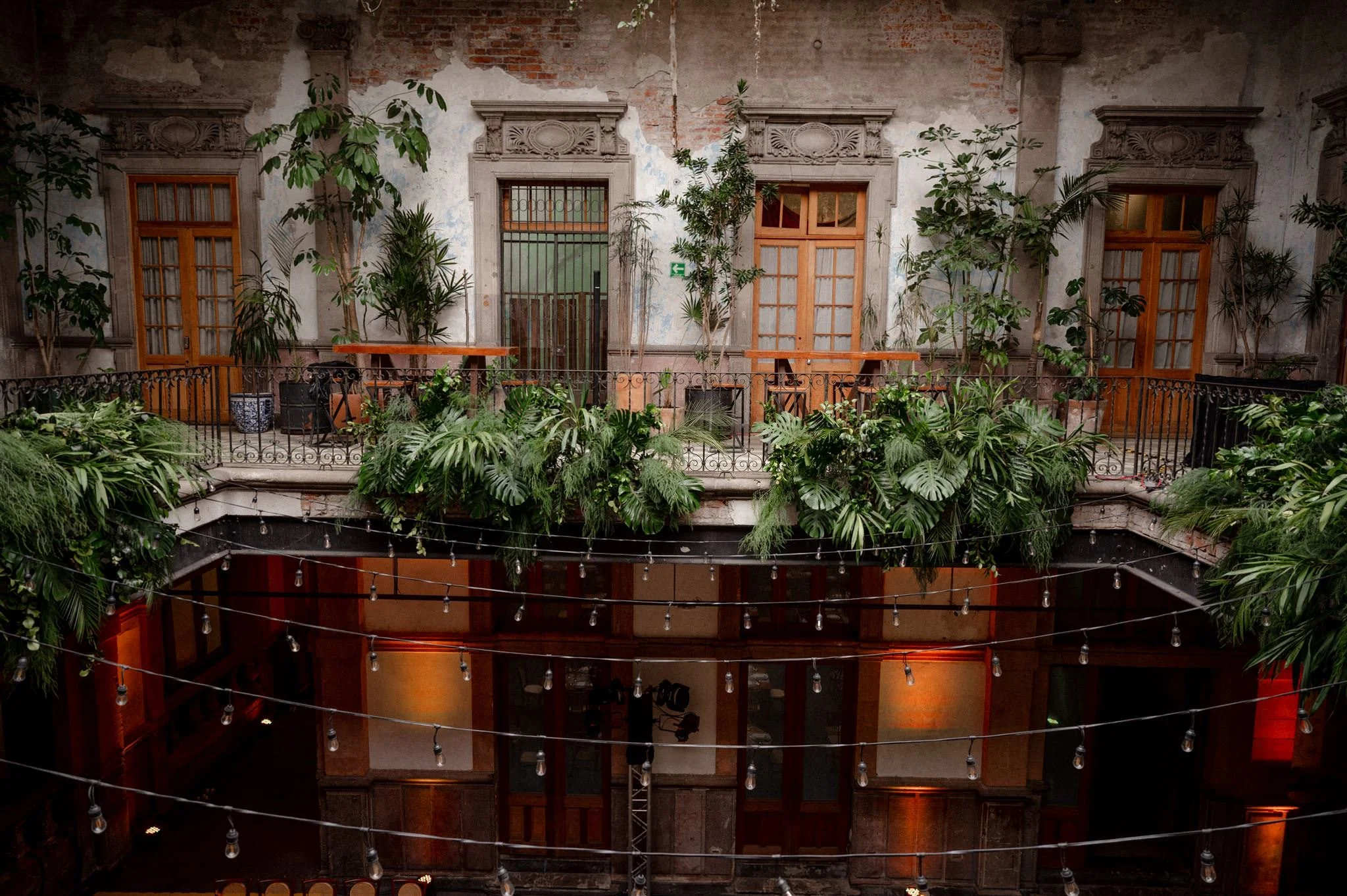 Romantic wedding venue at Proyectos Públicos: Prim in Mexico City, featuring a historic courtyard with aged brick walls, elegant balconies, lush greenery cascading over railings, and warm string lights creating an intimate, atmospheric setting.