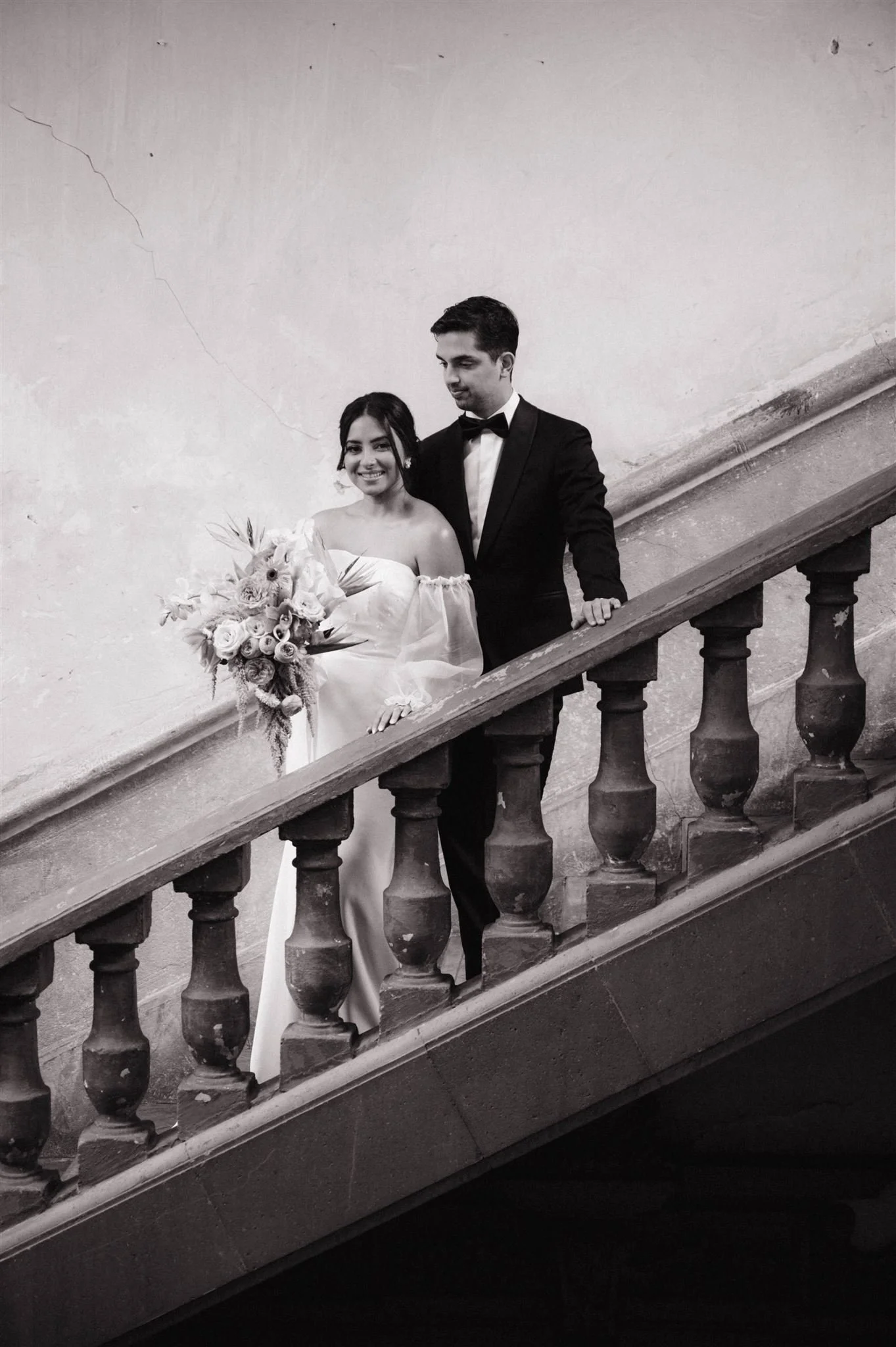 Bride and groom posing on a historic staircase at Proyectos Públicos: Prim in Mexico City, captured in a timeless black and white editorial wedding portrait