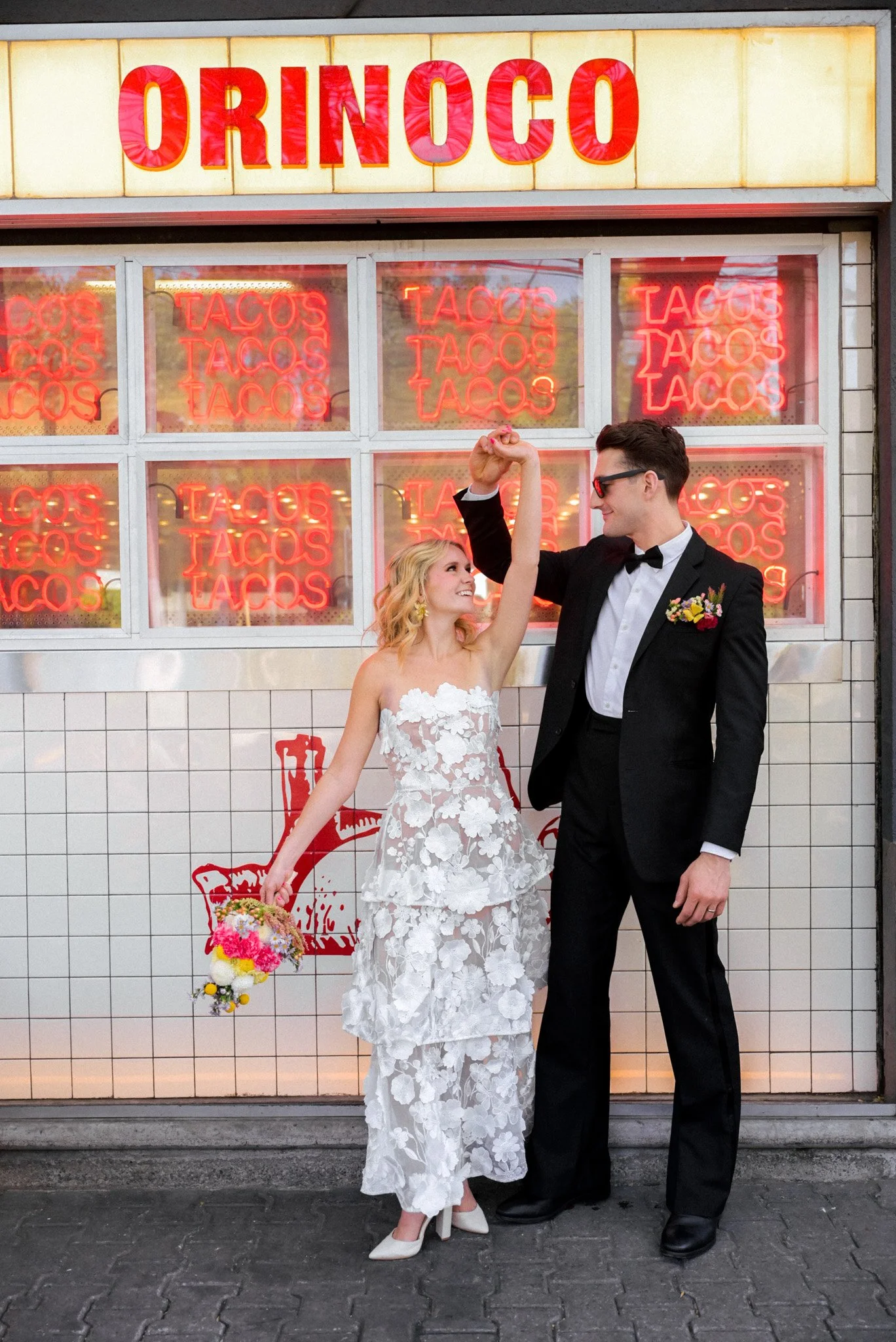 Bride and groom dancing in front of Tacos Orinoco in Mexico City, surrounded by bright neon signs and playful urban energy during their intimate elopement.