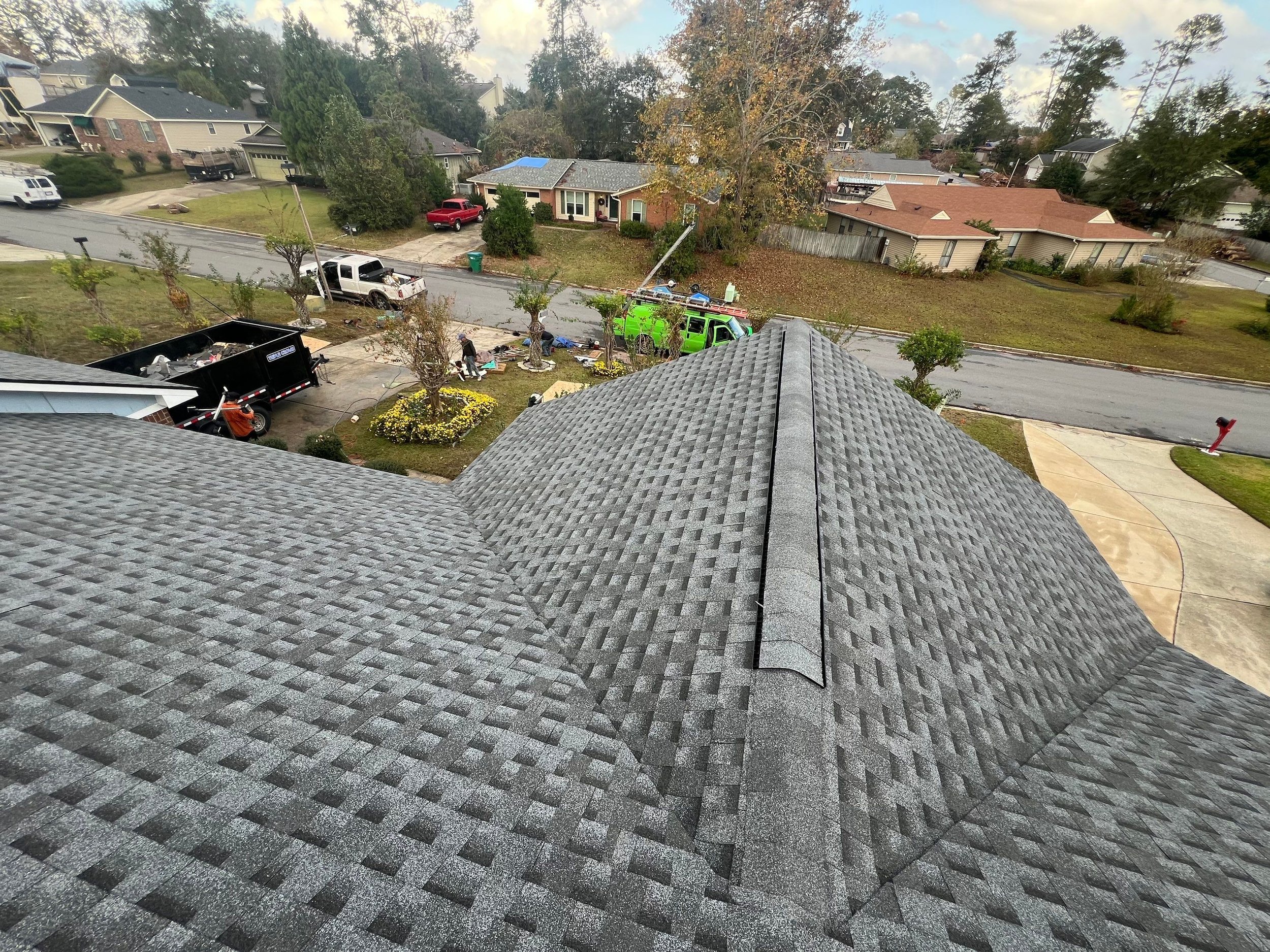 View from the roof of a house overlooking a residential neighborhood with construction or maintenance work happening in the yard below.