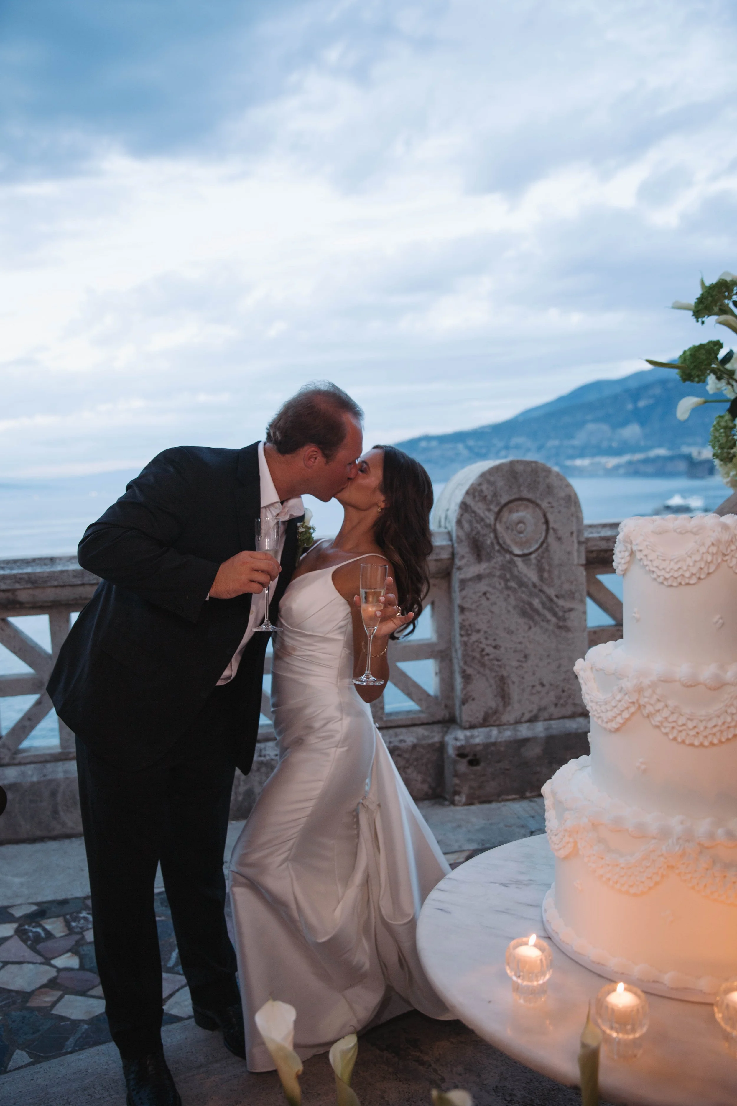 Bride and groom kissing beside their wedding cake at dusk at the Bellevue Syrene