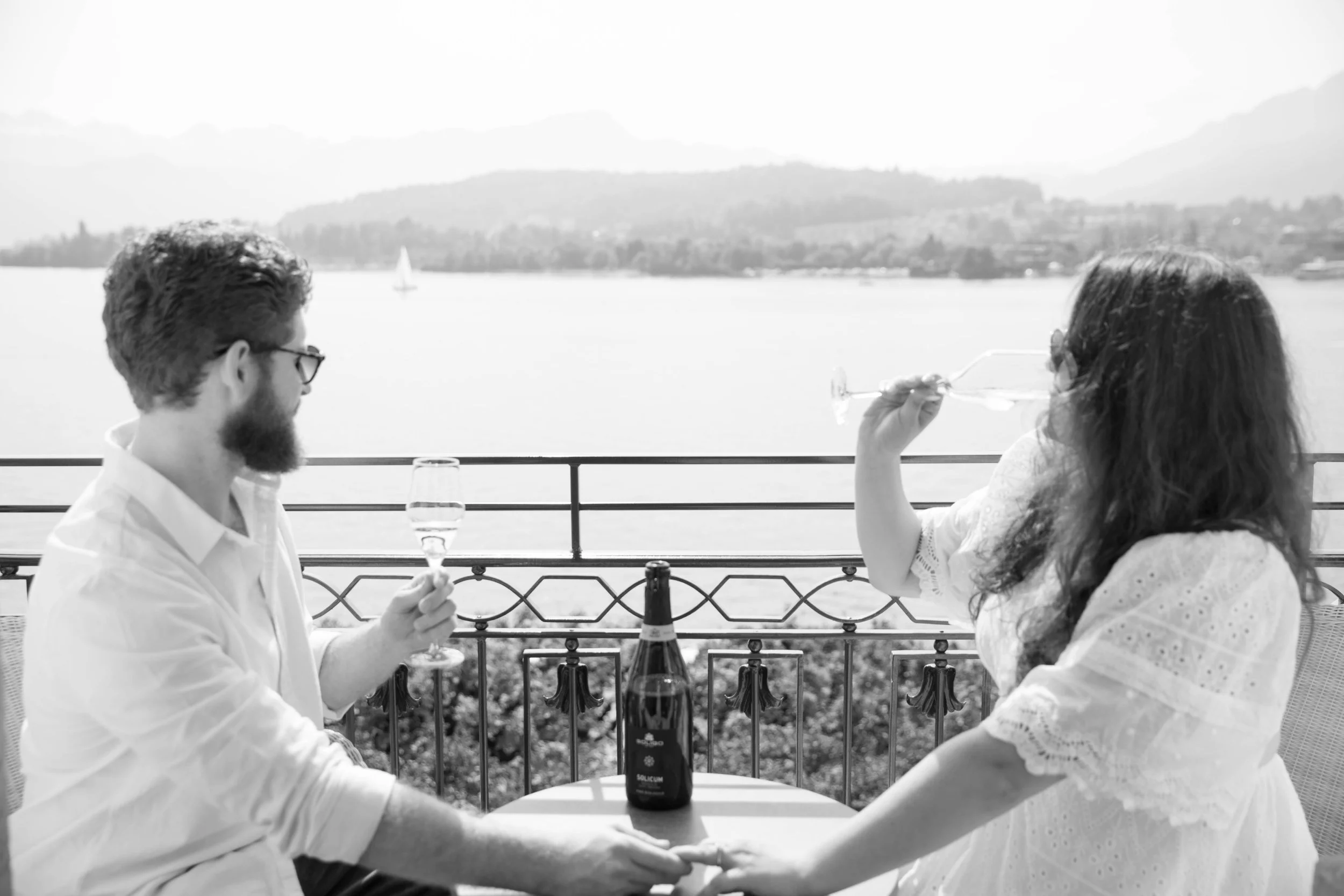 Black and white photo of a couple toasting champagne on a balcony above Lake Lucerne