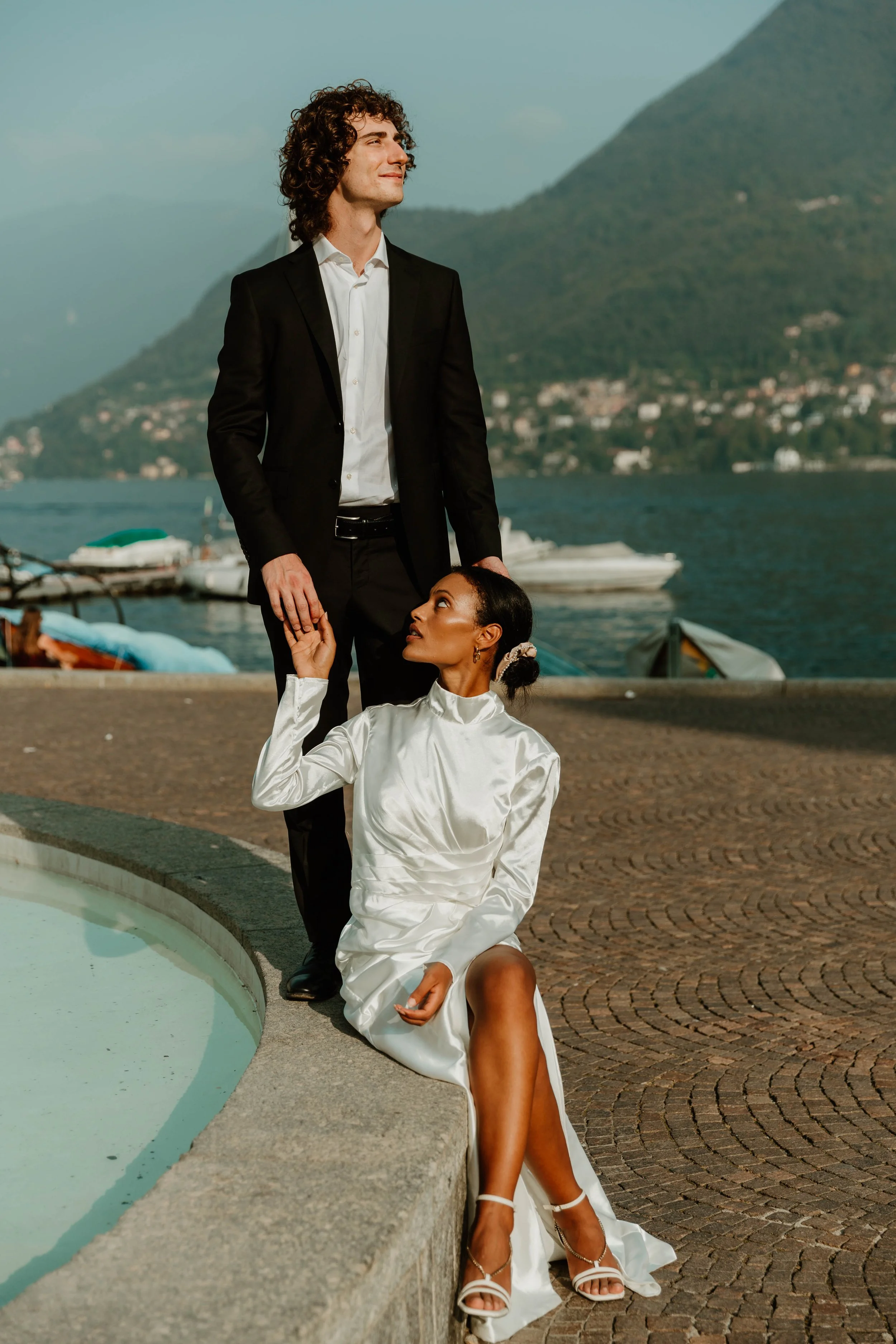 Bride seated on the fountain rim holding hands with groom on the Cernobbio lakefront