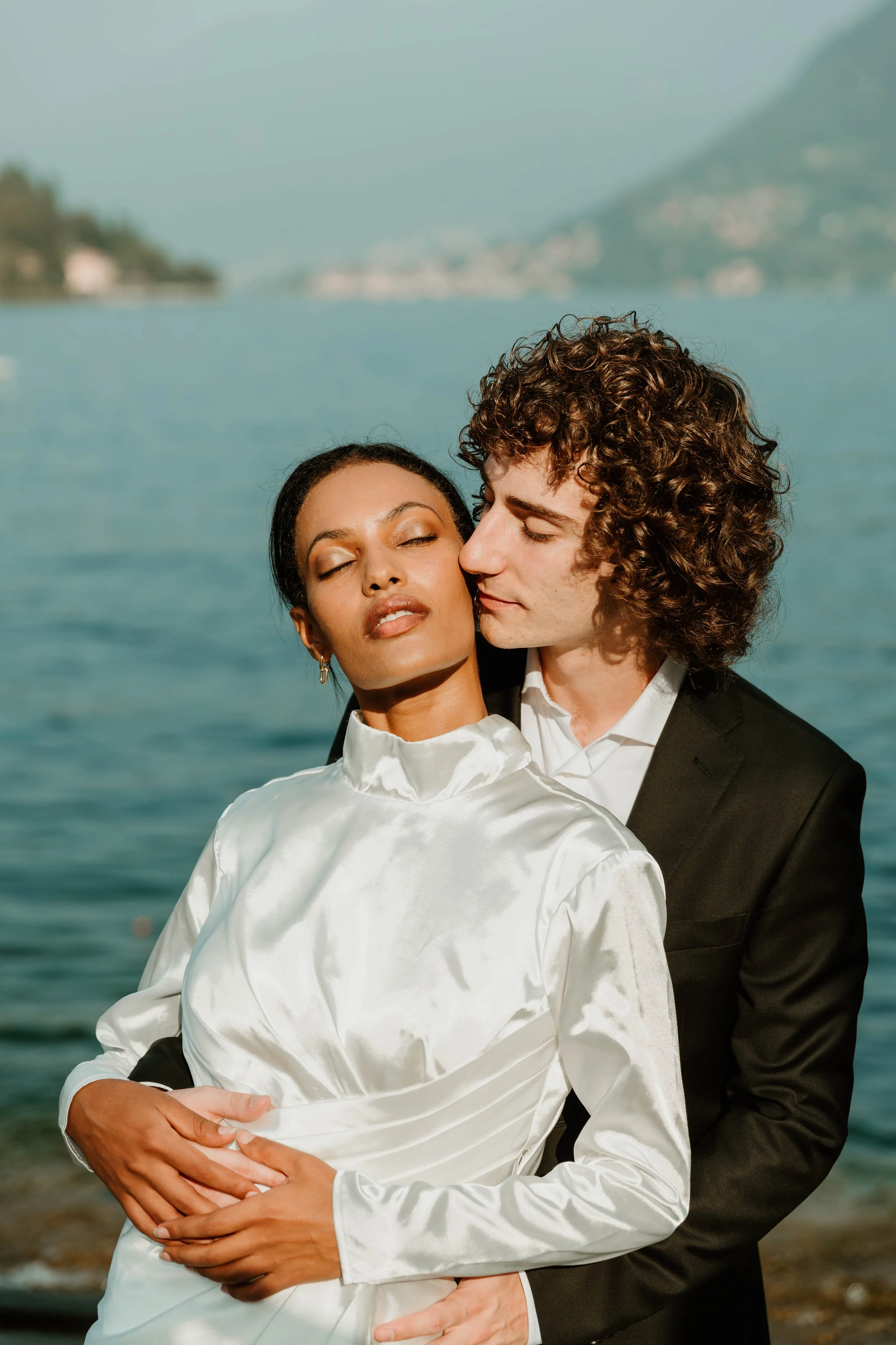 Groom holding the bride from behind at the edge of Lake Como at golden hour