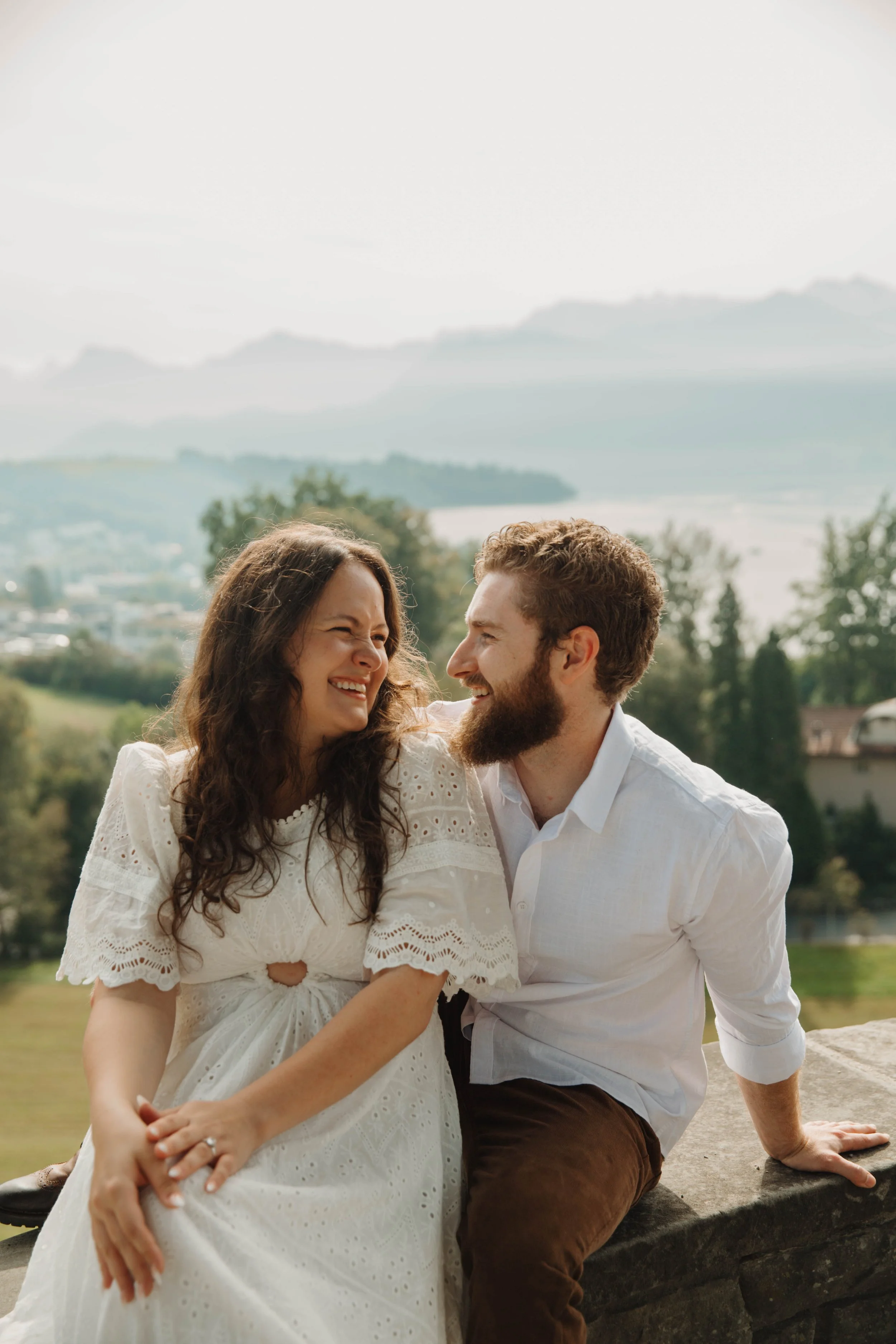 Couple laughing on a stone wall at a garden viewpoint above Lucerne, Switzerland