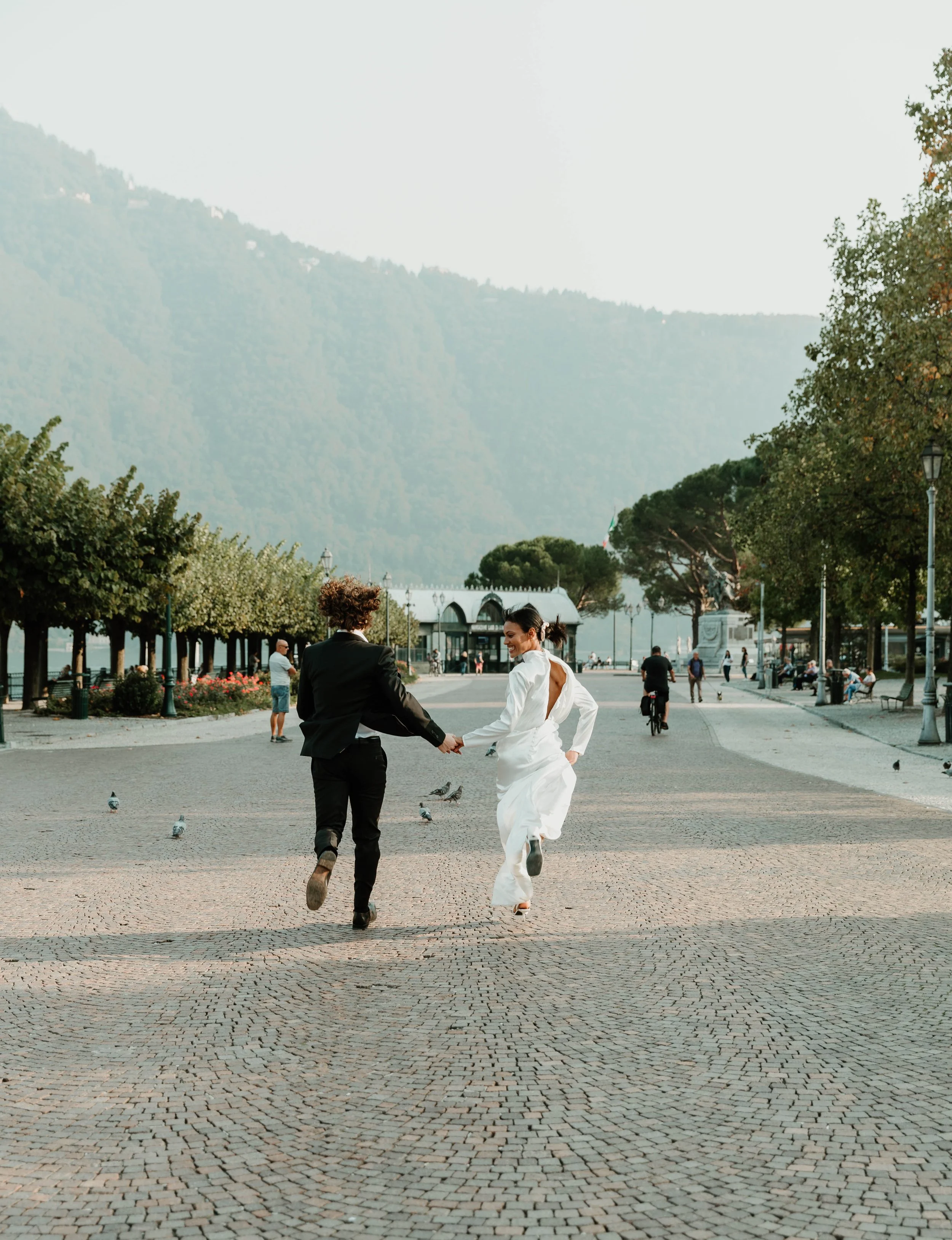 Bride and groom running down the tree lined lakeside promenade in Cernobbio on Lake Como