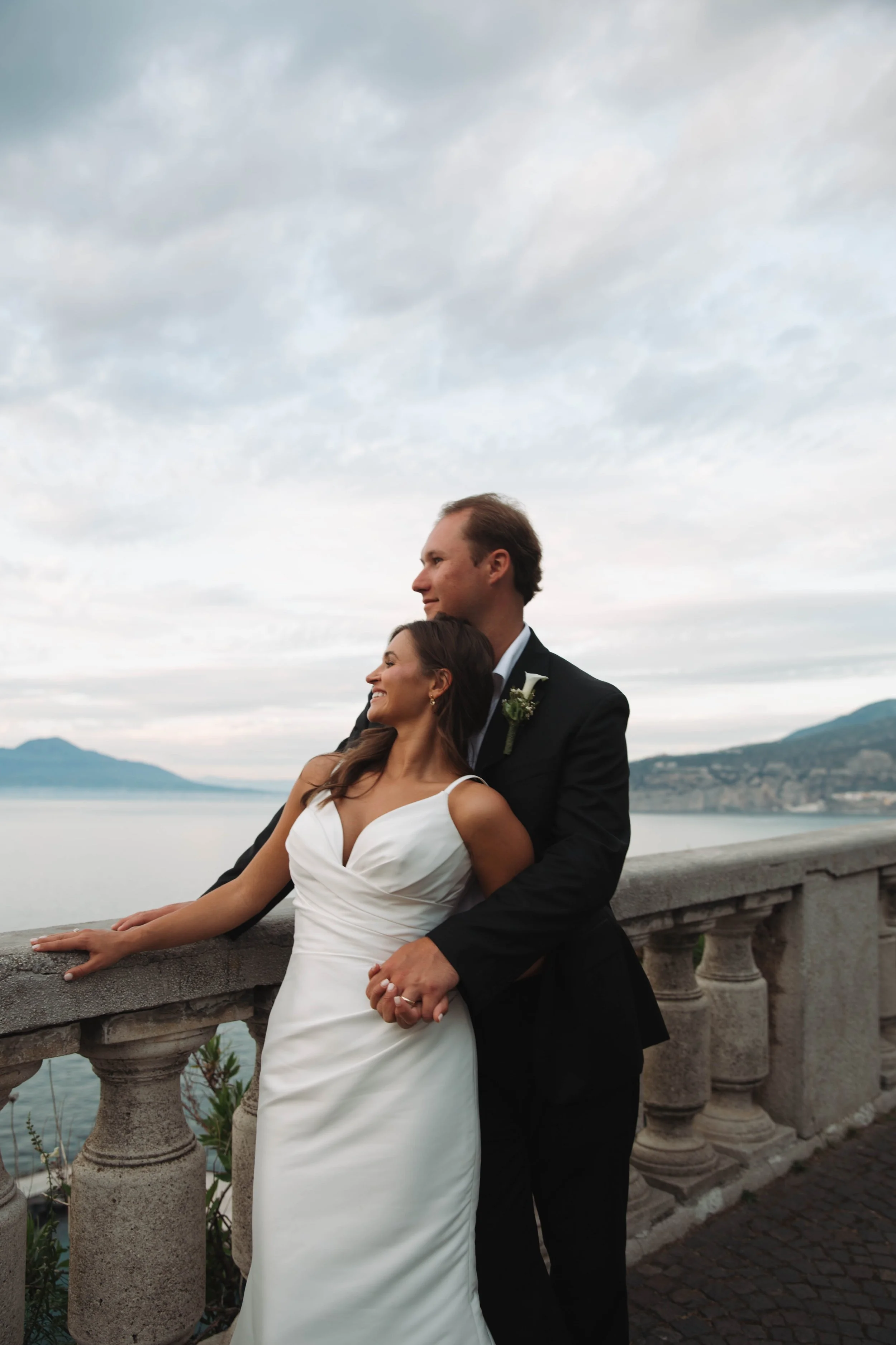 Newlyweds leaning on the stone balustrade at the Bellevue Syrene with Mount Vesuvius across the bay
