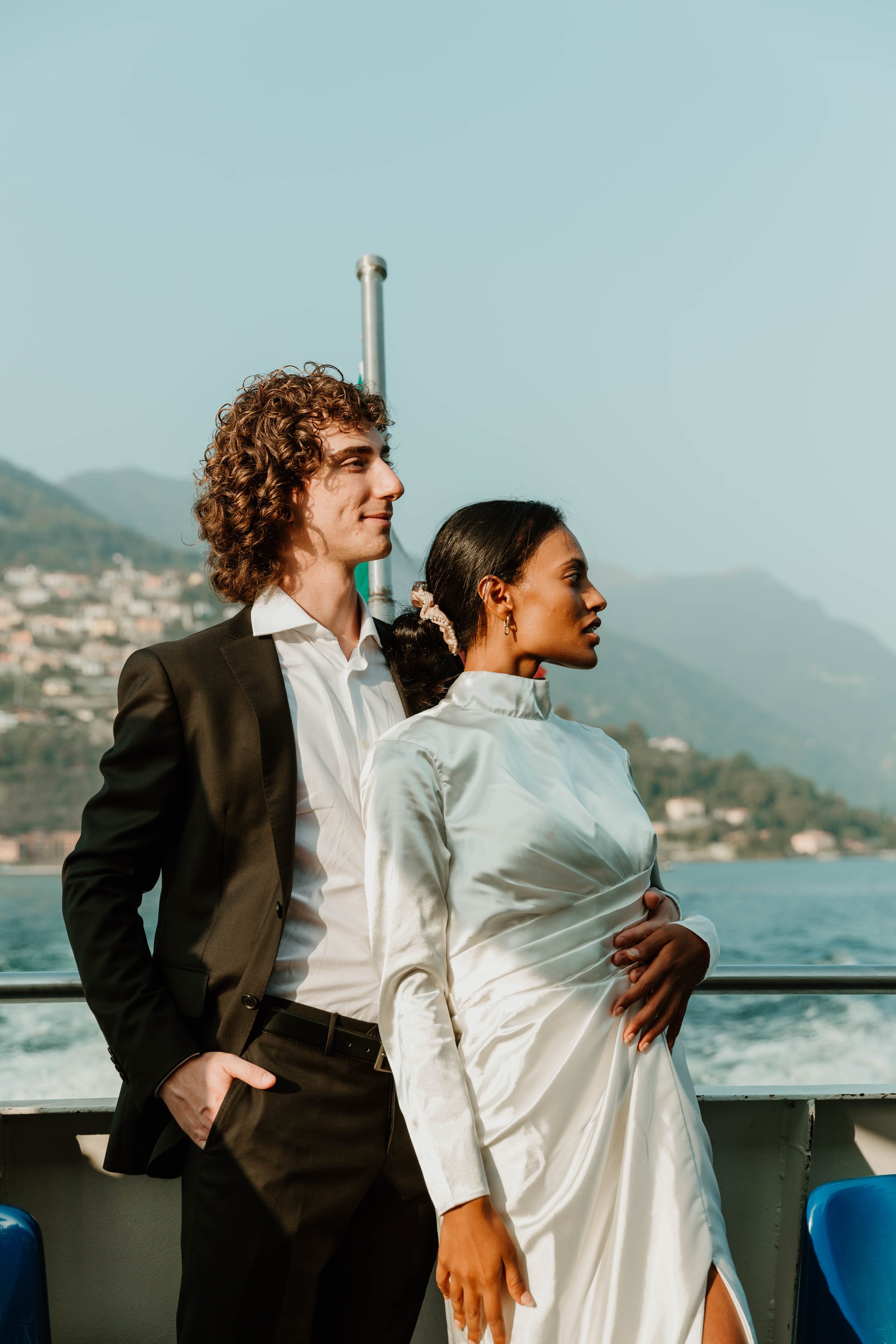 Groom holding bride at the ferry railing with the hills of Lake Como behind them