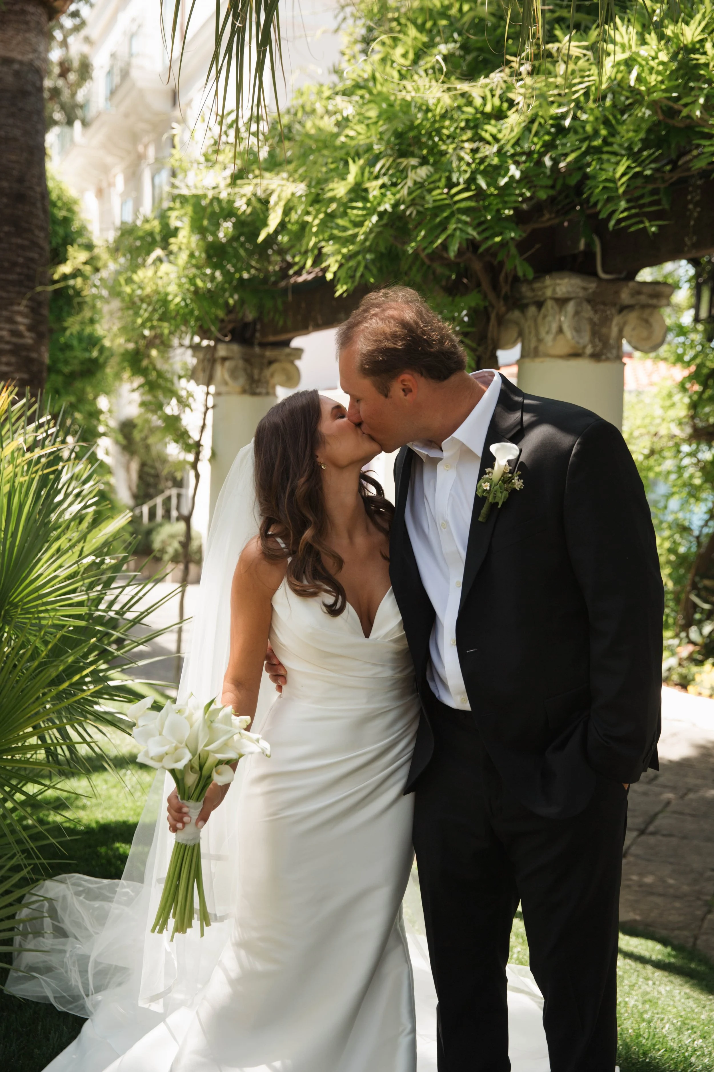Bride and groom kissing under the wisteria pergola in the Bellevue Syrene gardens