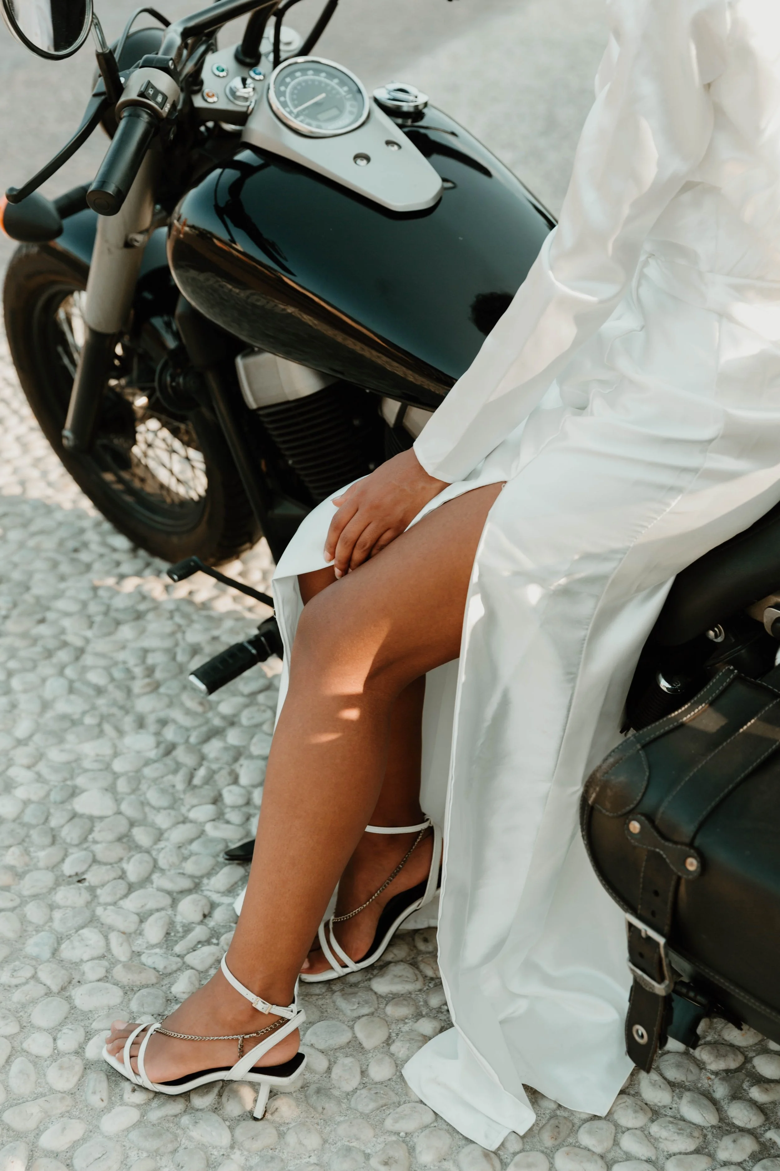 Detail of the bride's heels and silk gown while seated on a black motorcycle in Cernobbio