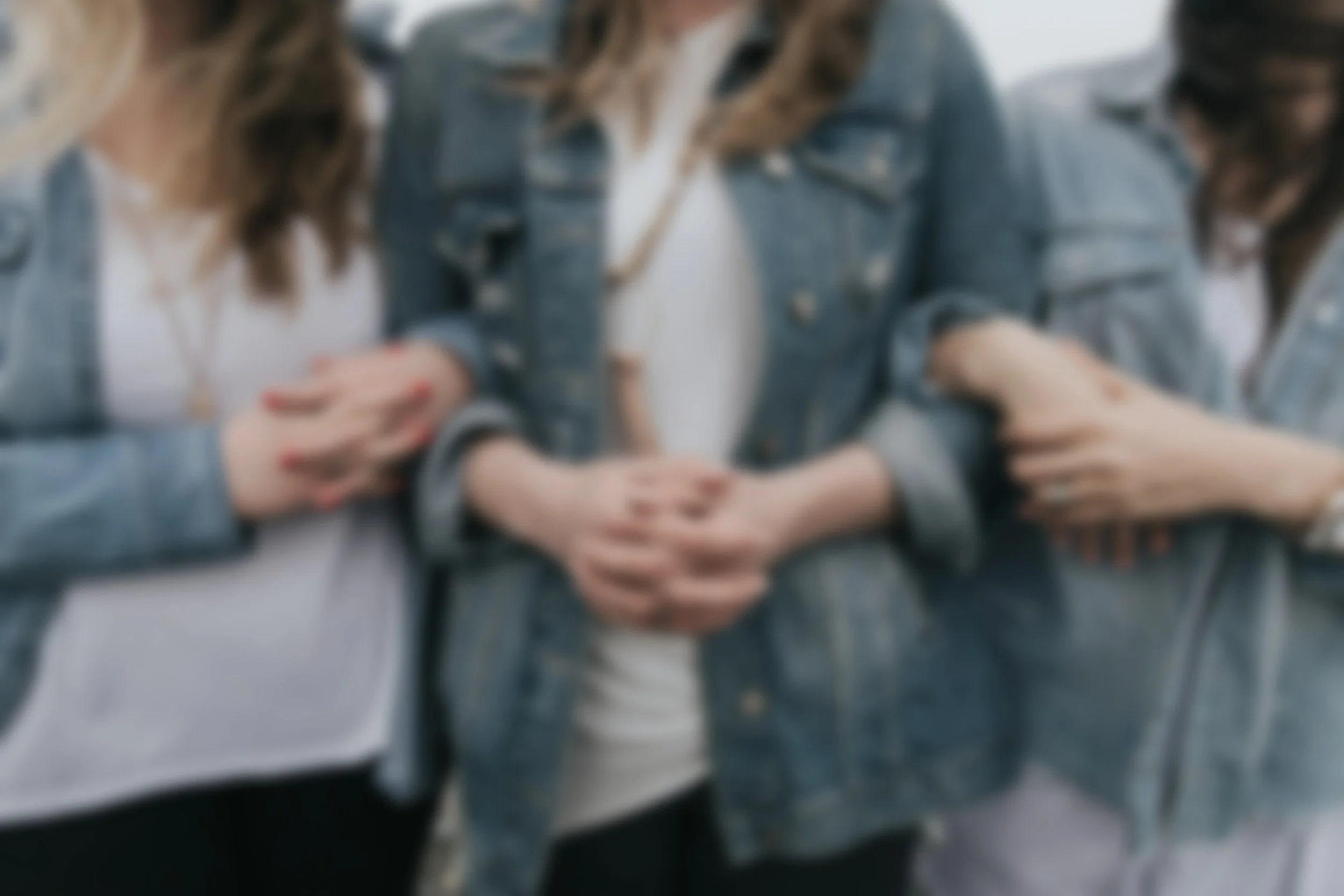 group of 3 women in jean jackets and white t-shirts linking arms