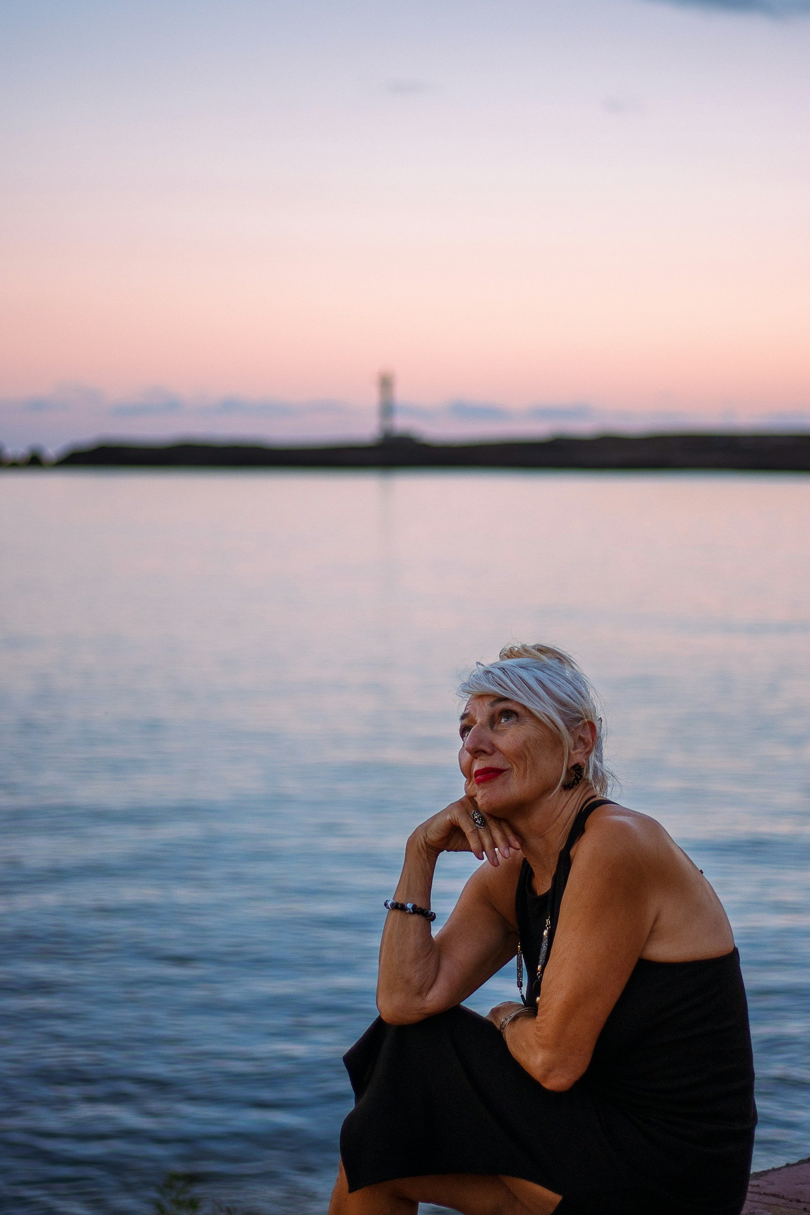 woman with white hair and red lipstick sitting by a lake looking hopeful after anxiety therapy