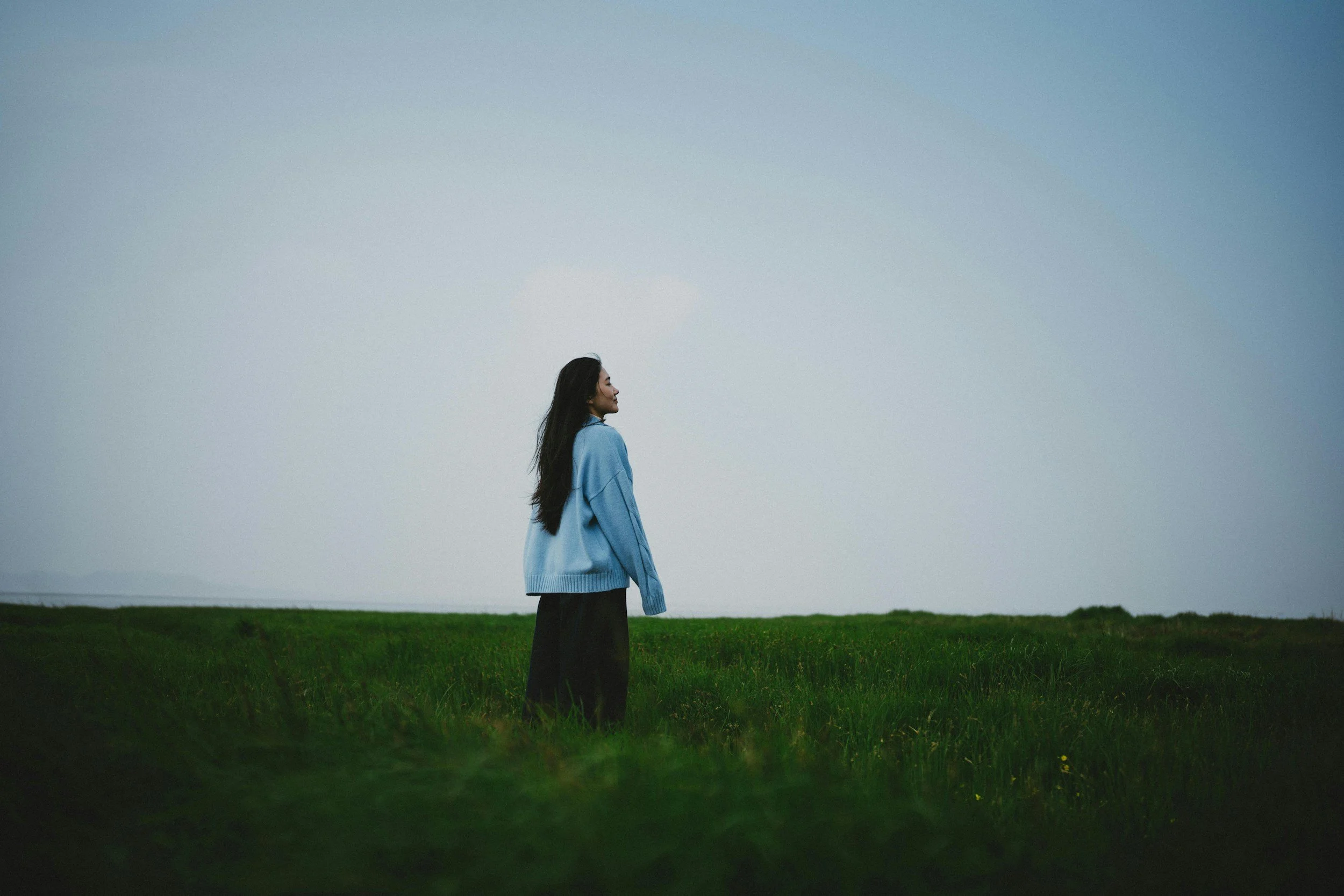 woman with long black hair in blue sweatshirt standing in grass
