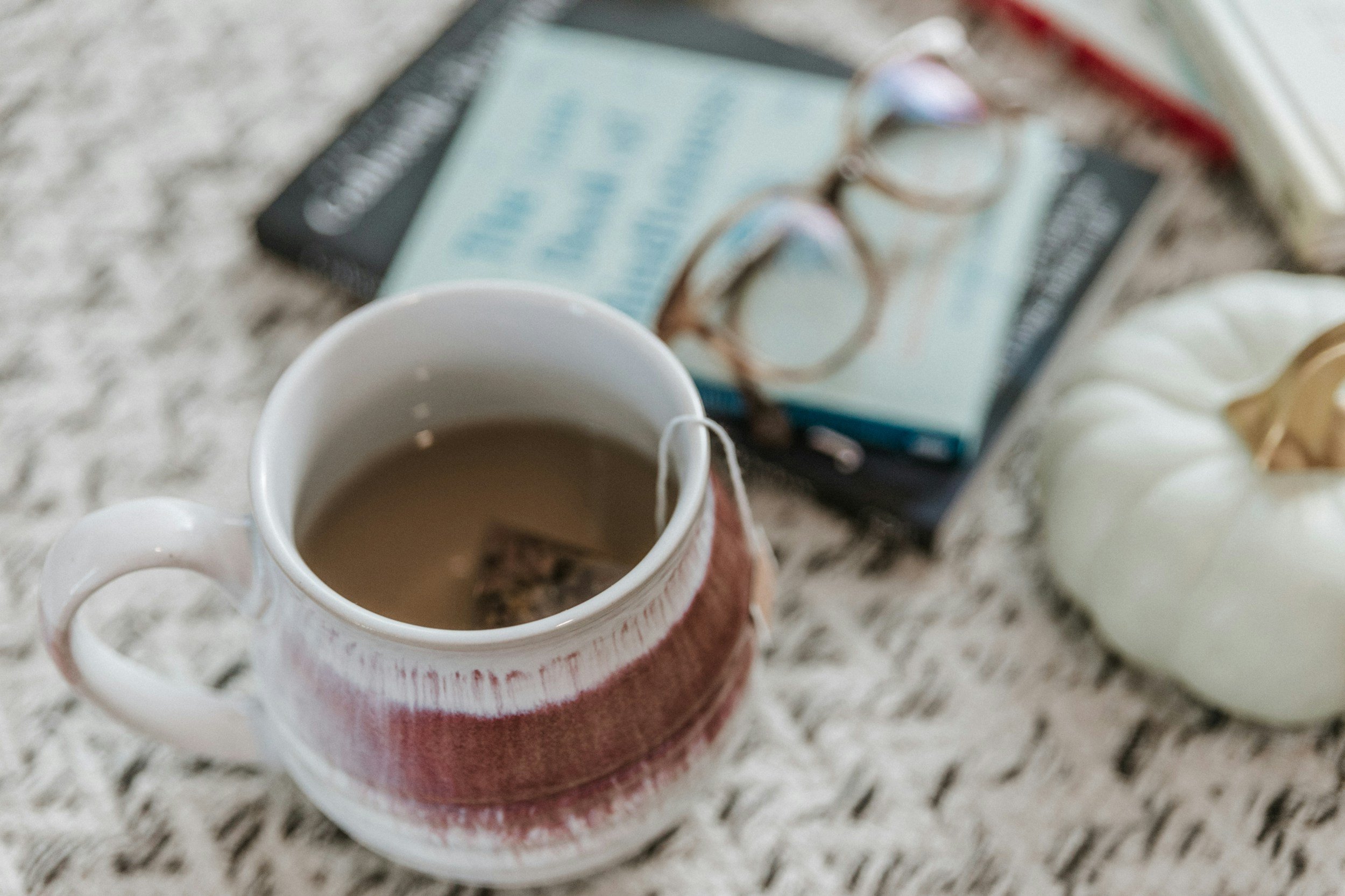 warm mug of tea on cream colored ottoman next to glasses and book - autistic burnout vs depression blog from Amanda Morris Therapy